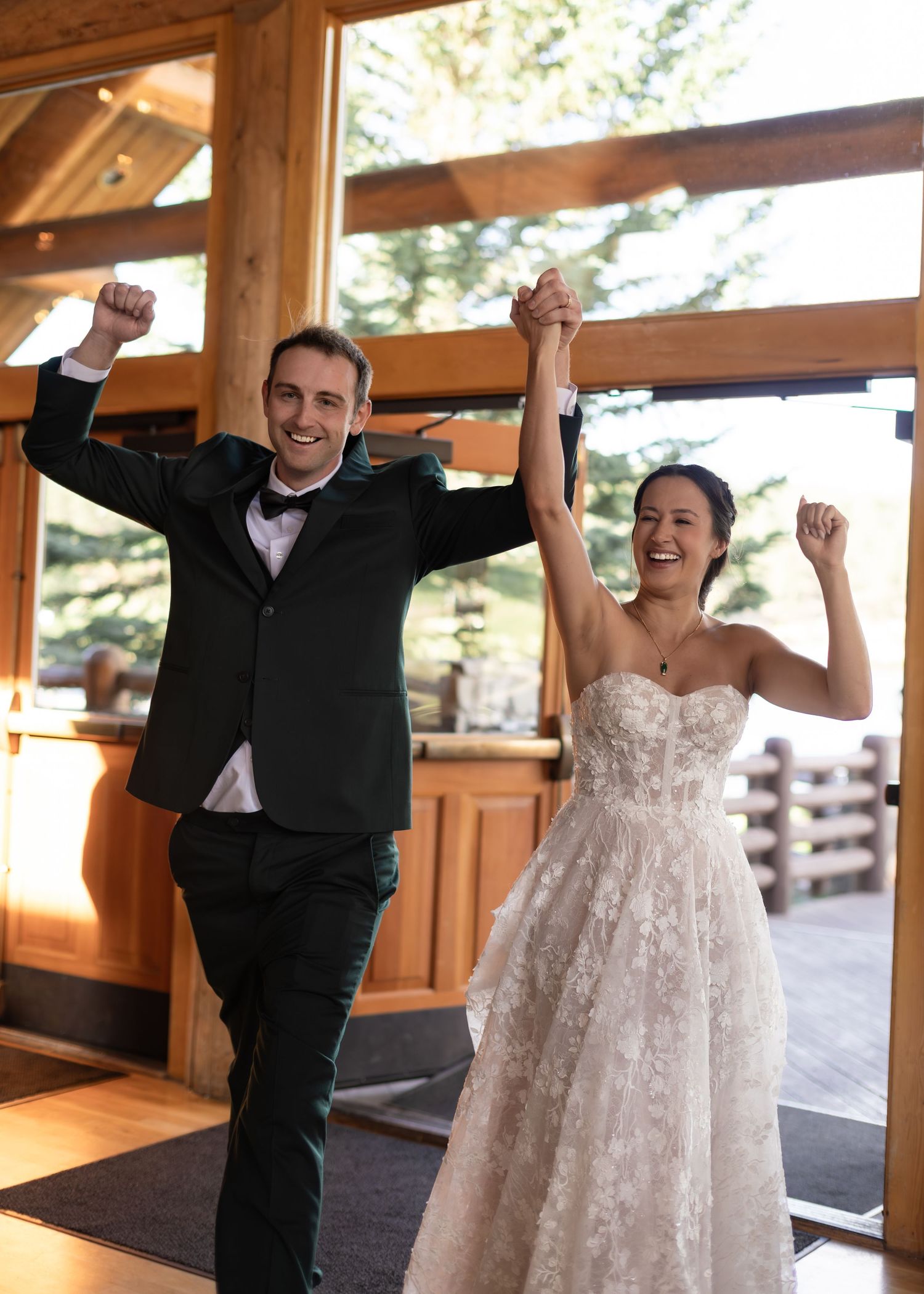 Joyful newlyweds celebrate their grand entrance raising hands at rustic wedding venue.