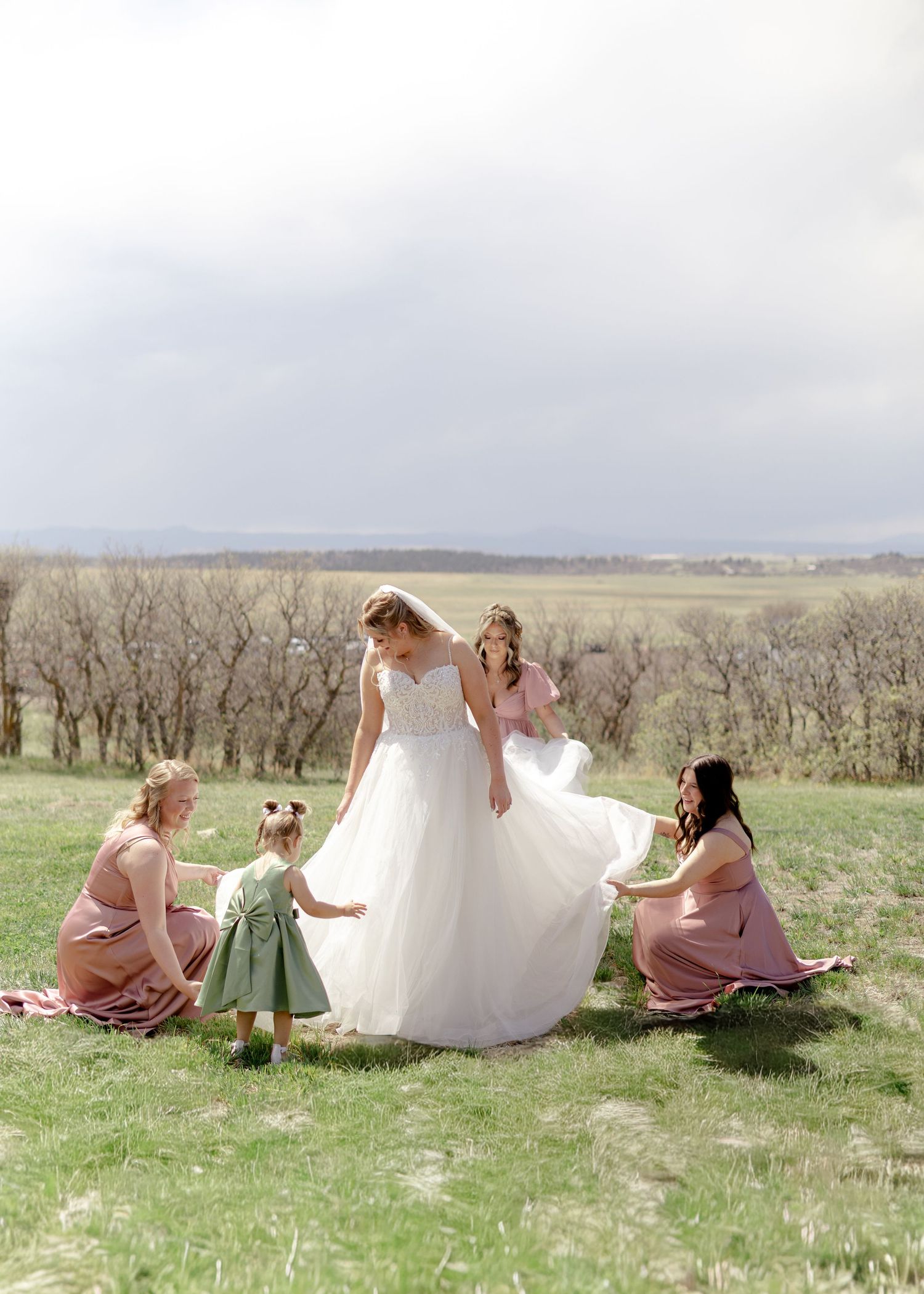 Bride in white ballgown surrounded by bridesmaids in pink dresses and flower girl outdoors.