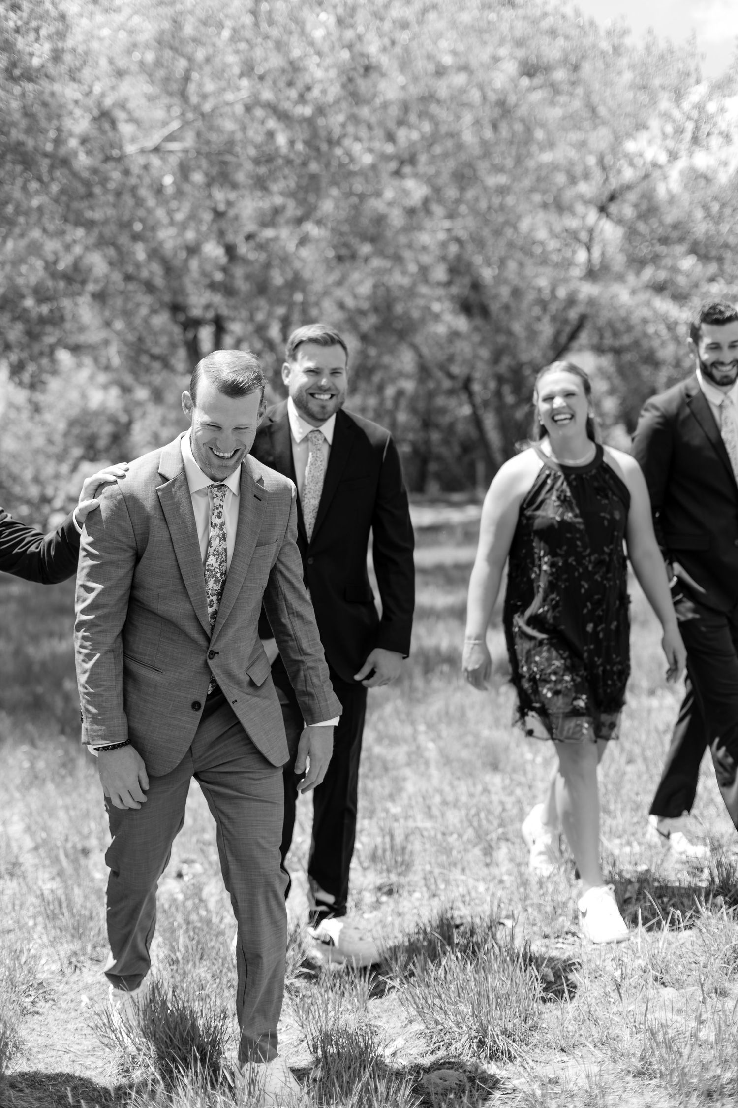 Wedding party walks through a field laughing in black and white outdoor photo.