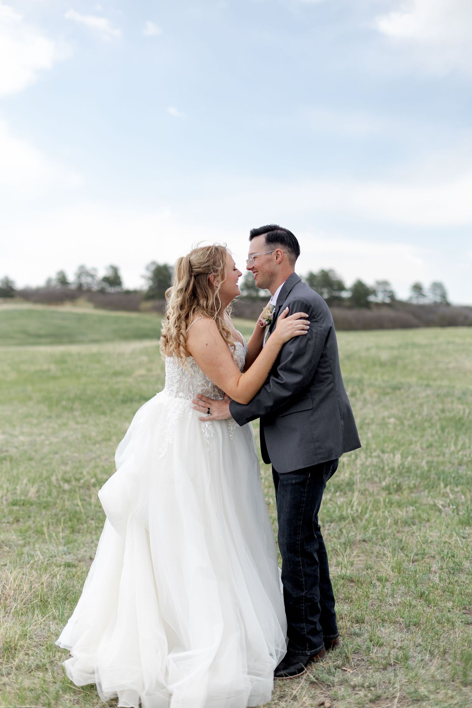 Bride and groom embracing and smiling at each other in an open green field.