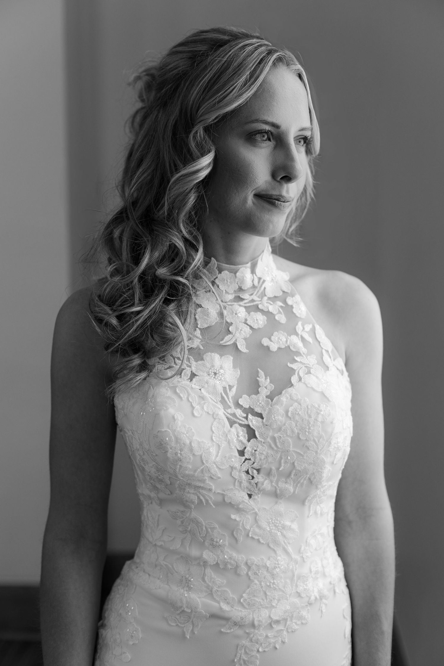 Black and white portrait of a bride in a high-neck lace halter wedding gown with floral applique details.