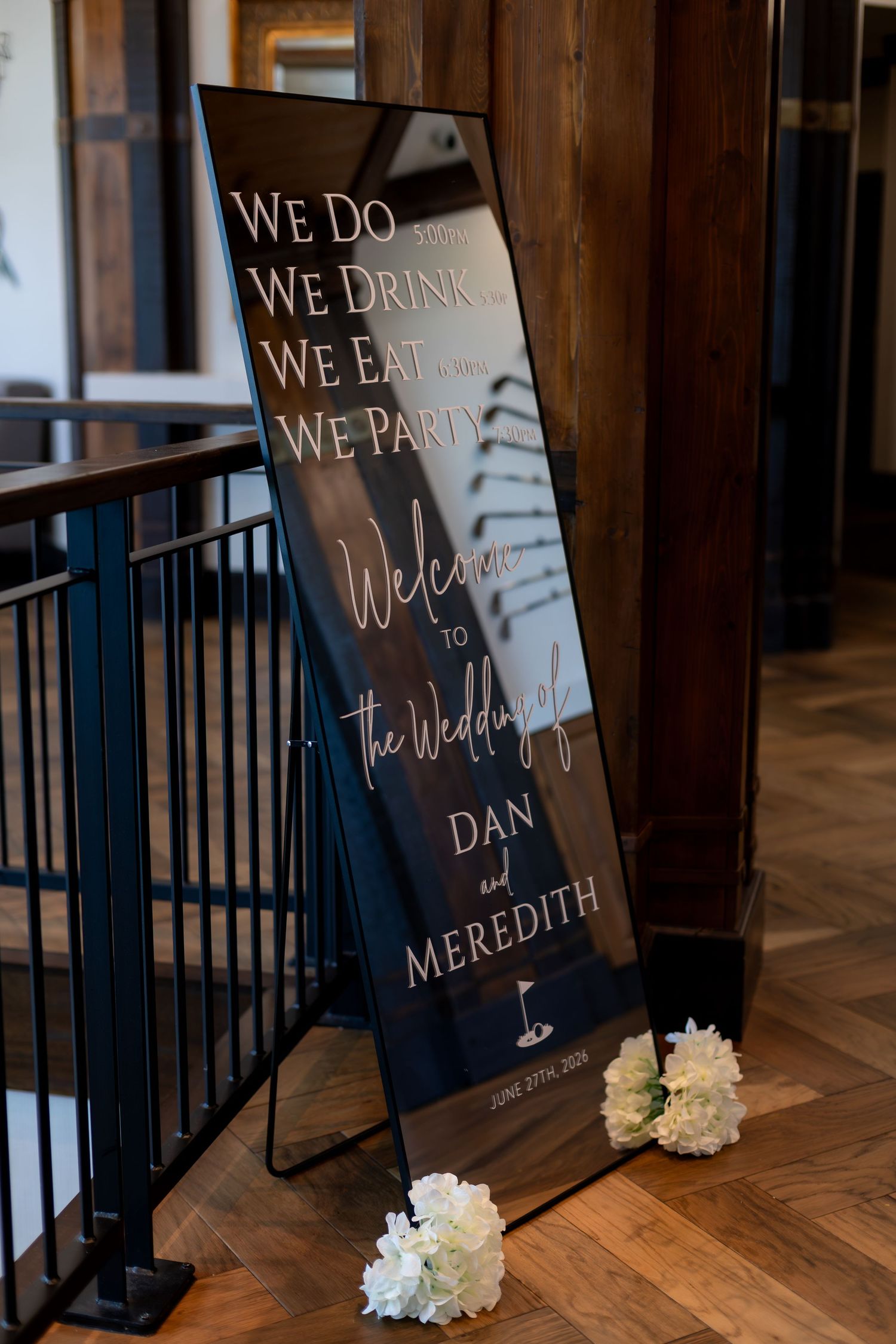 Elegant black wedding welcome sign for Dan and Meredith with white floral accents on wooden floor.