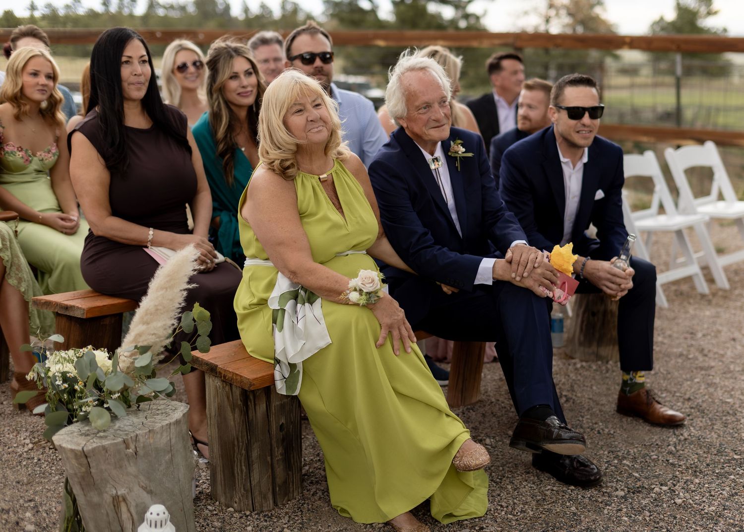 Wedding guests in colorful attire seated at outdoor ceremony, smiling and watching the proceedings.