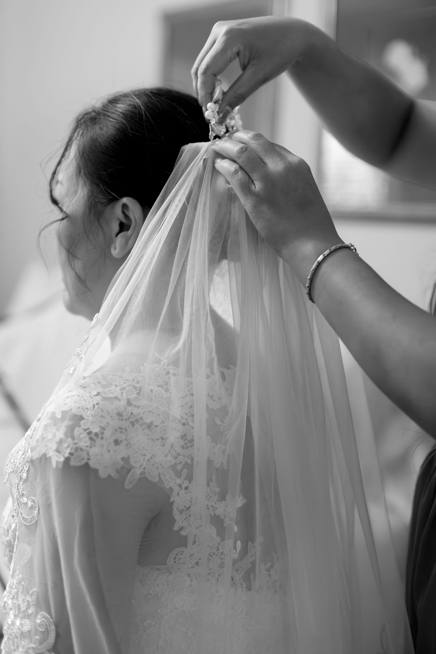 Black and white photo of a bride having her wedding veil pinned into her updo hairstyle by a bridesmaid.