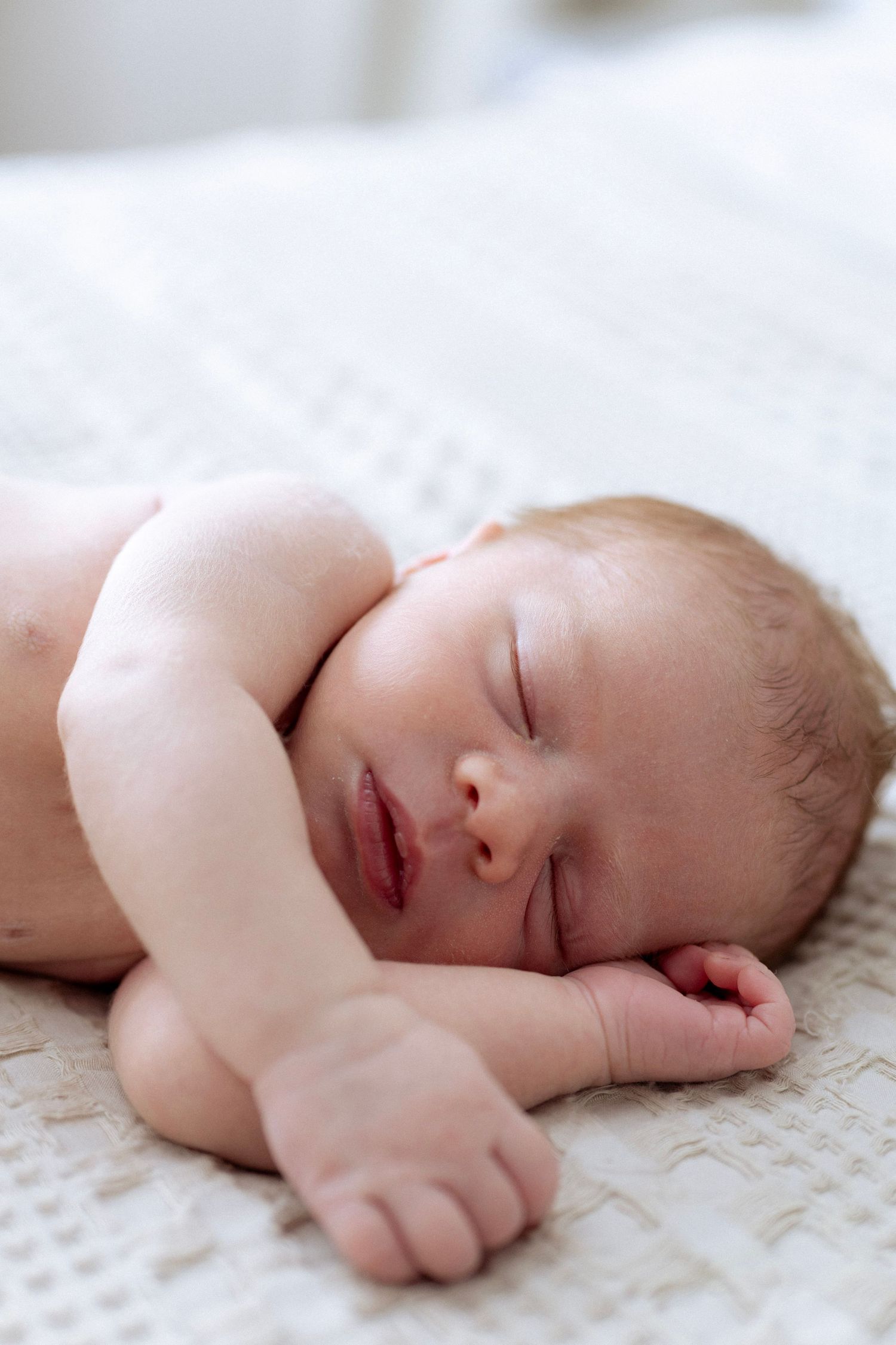 Sleeping newborn baby lying on soft white textured blanket in natural light.