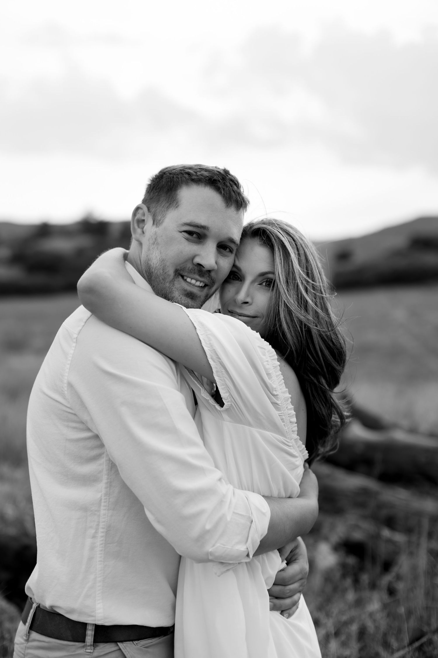 Couple embracing tenderly in a field, black and white portrait photography.