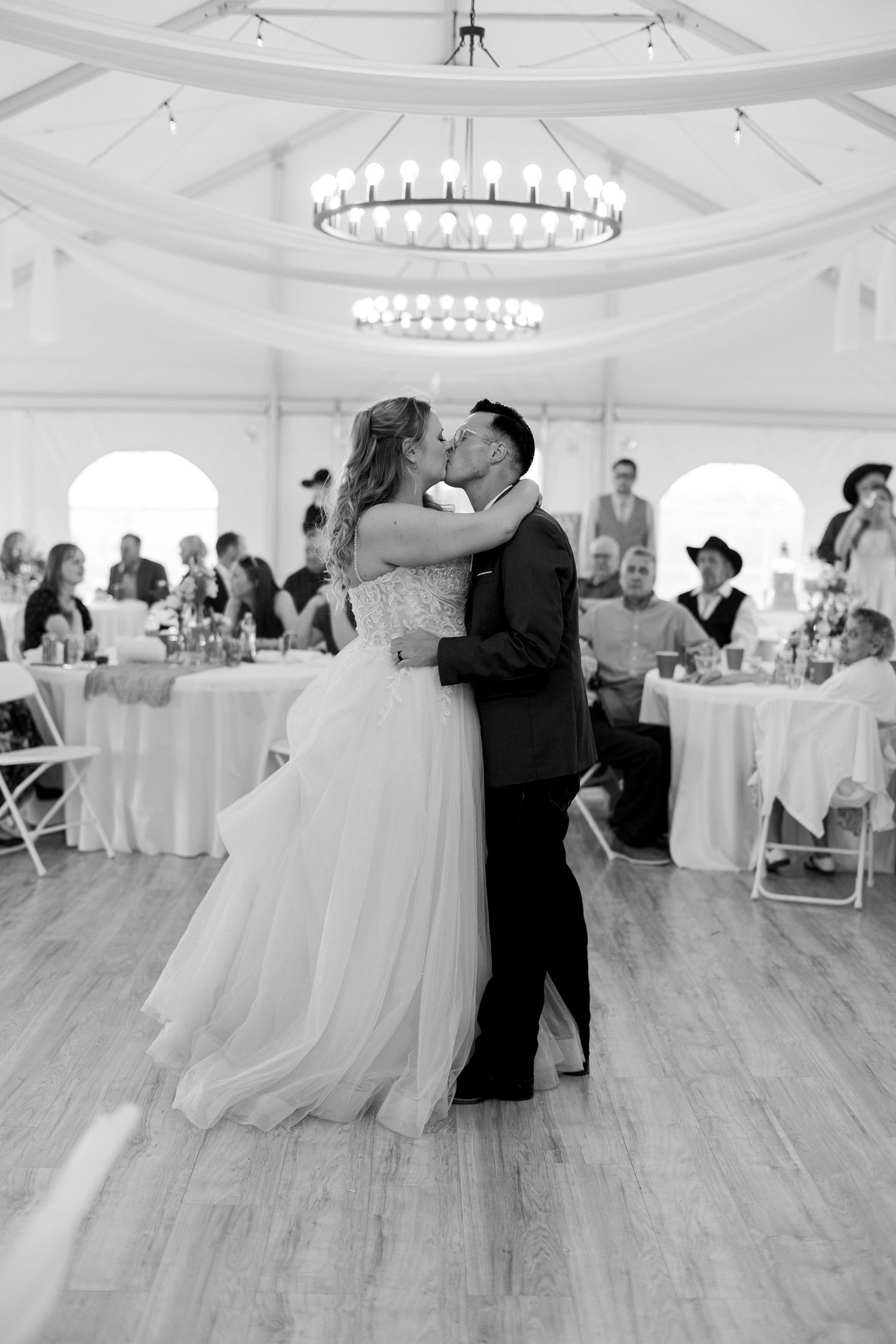 Black and white photo of a bride and groom sharing their first dance kiss at a wedding reception.