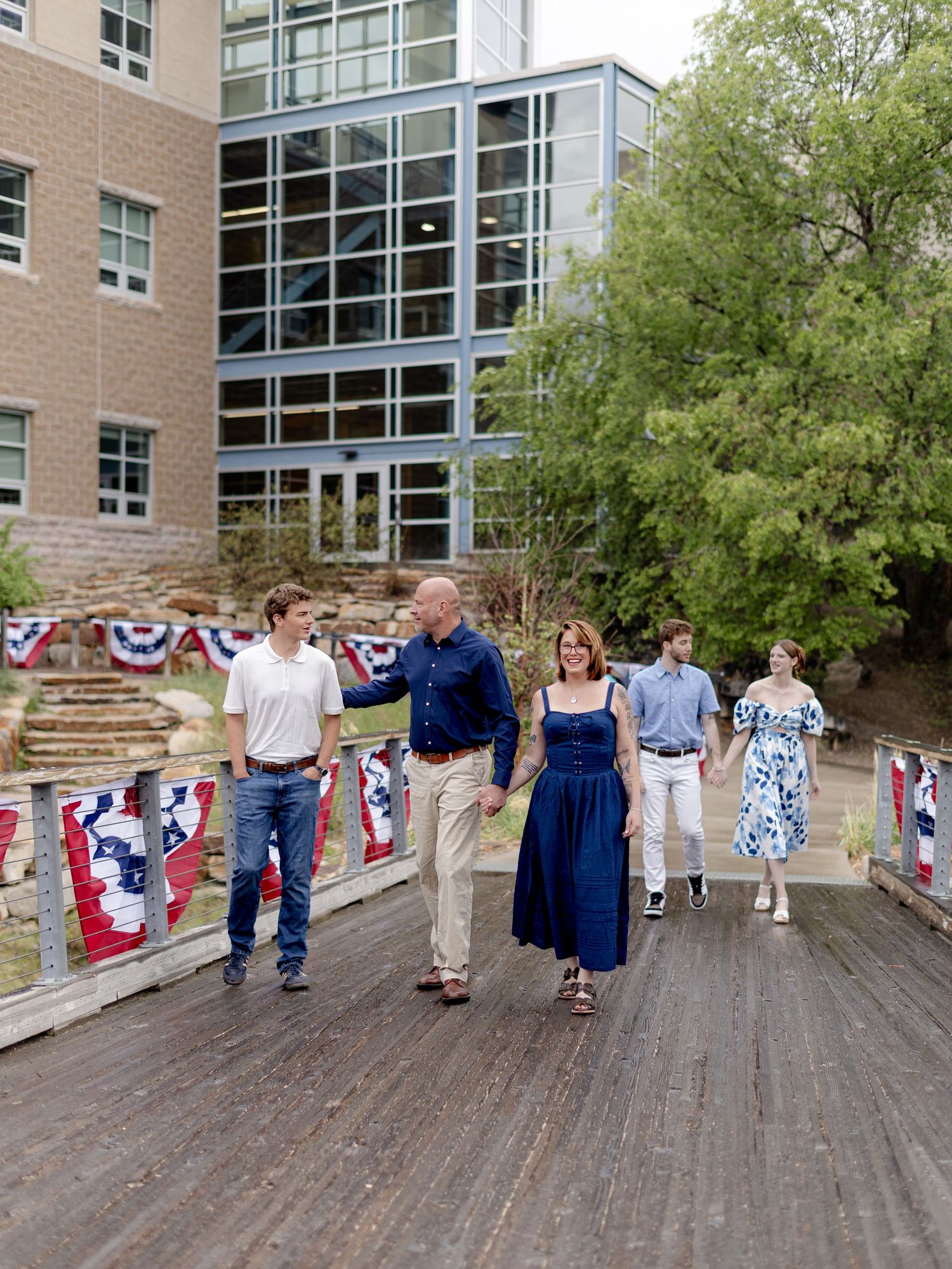 Family walking on wooden deck with patriotic bunting decorations outside a modern brick building.