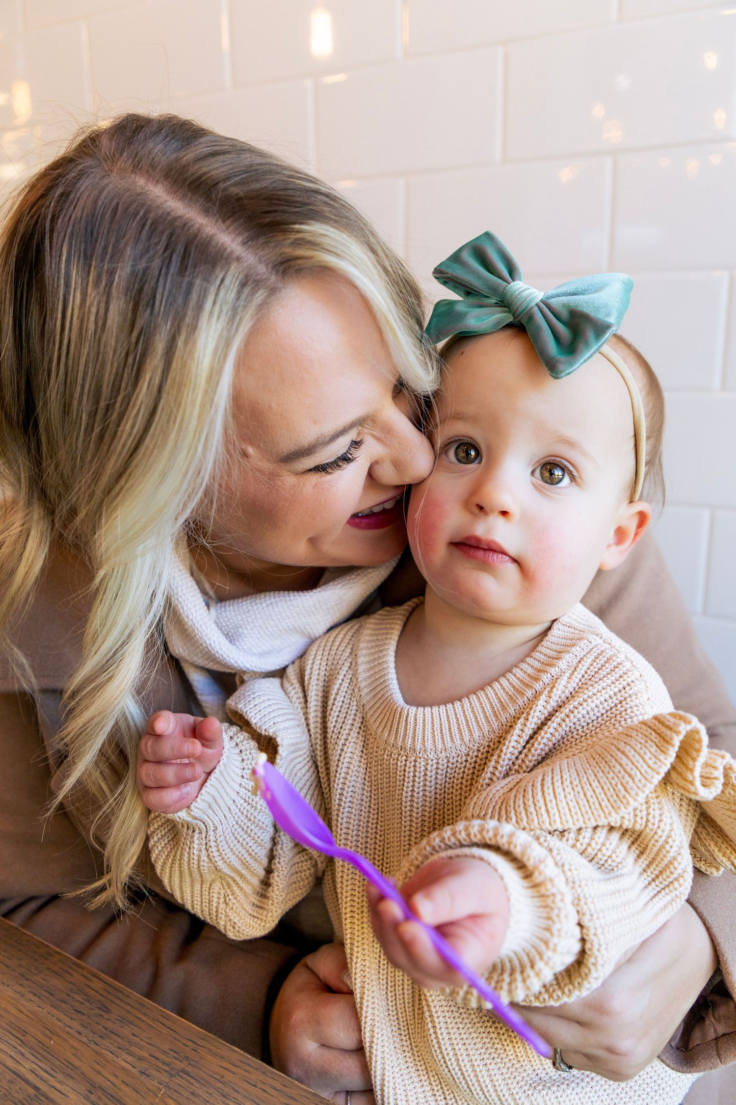 A parent and child share a sweet moment while wearing matching beige sweaters in a photo series.