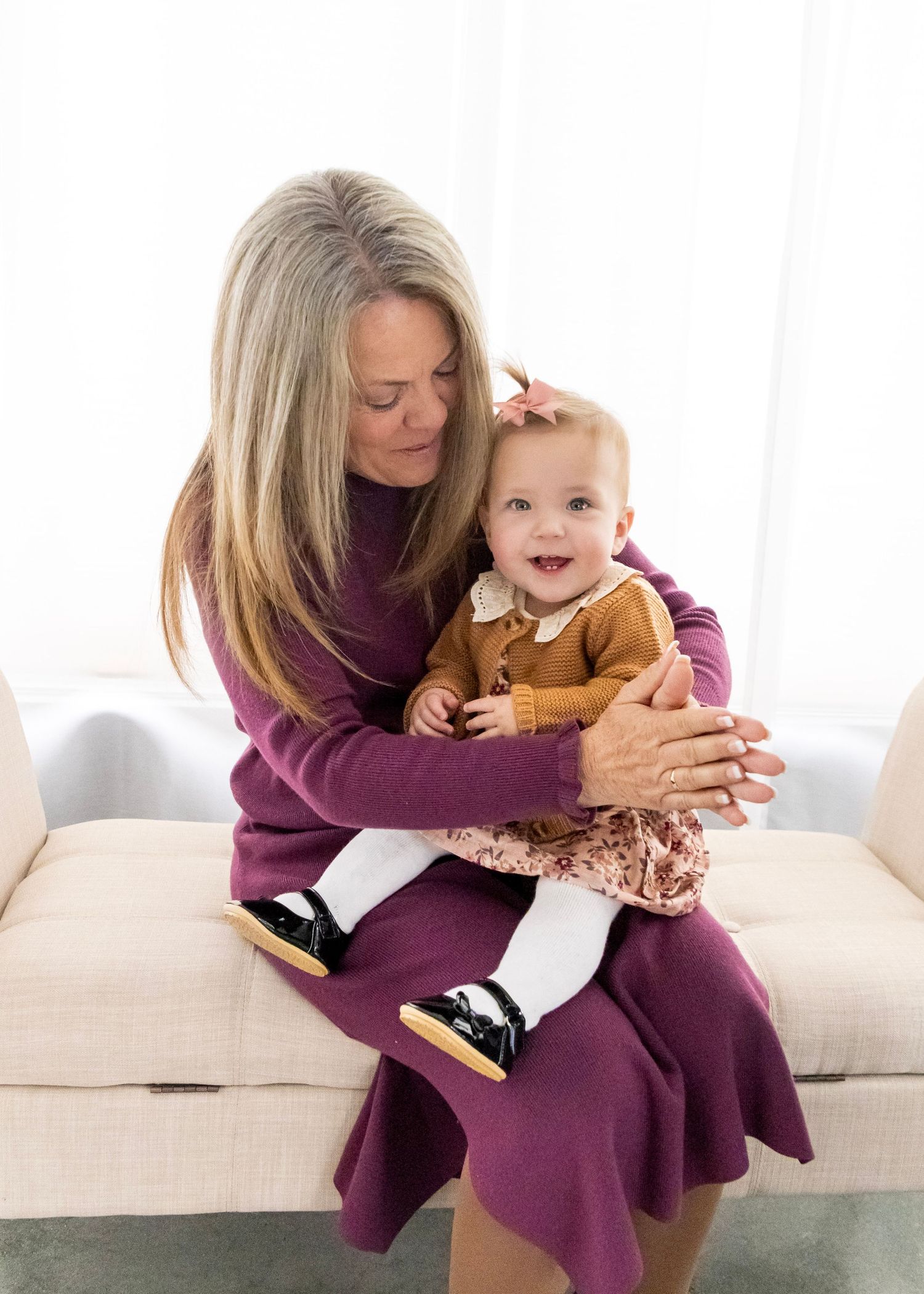 A person in a purple dress sits on a couch playing and interacting with a small child wearing brown clothing.