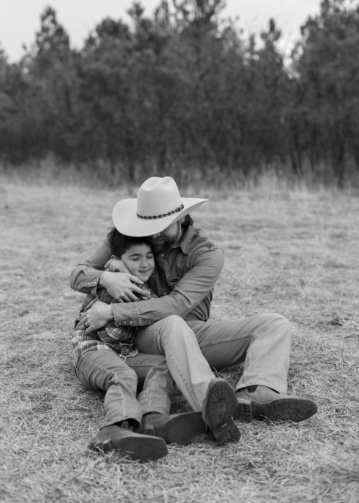A person in cowboy attire demonstrates proper shooting stance while lying prone on grassy ground.