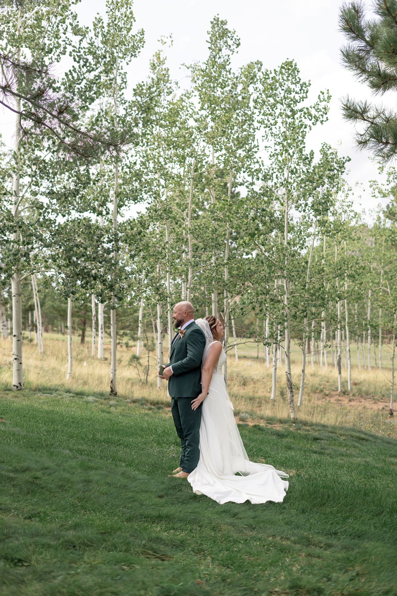 Bride and groom share a romantic moment on green lawn surrounded by white birch trees in an outdoor wedding setting.
