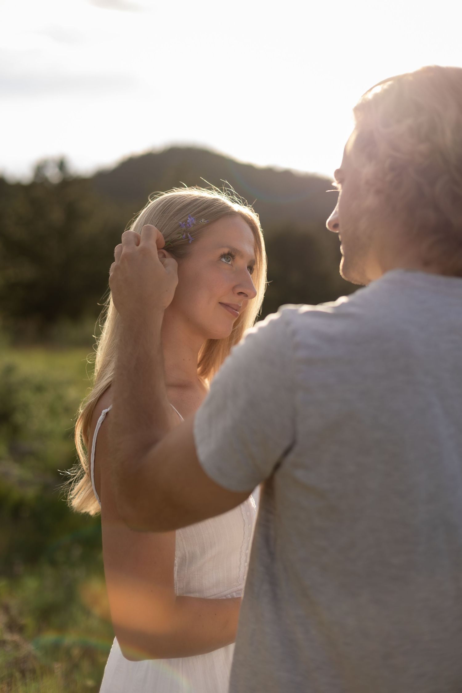 A man gently tucks hair behind a woman's ear during a romantic golden hour moment outdoors.