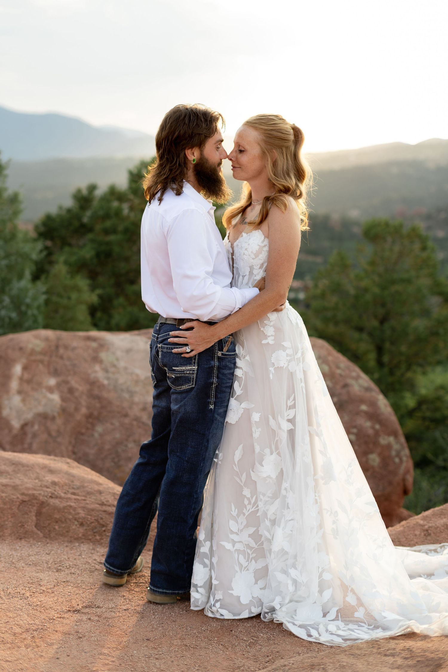 A bride and groom share a romantic kiss in wedding attire at Garden of the Gods with mountain views at sunset.