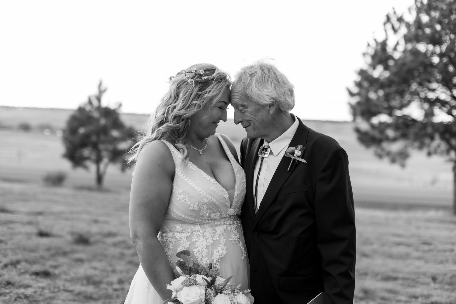 Bride and older gentleman share tender forehead touch moment in black and white wedding photo.