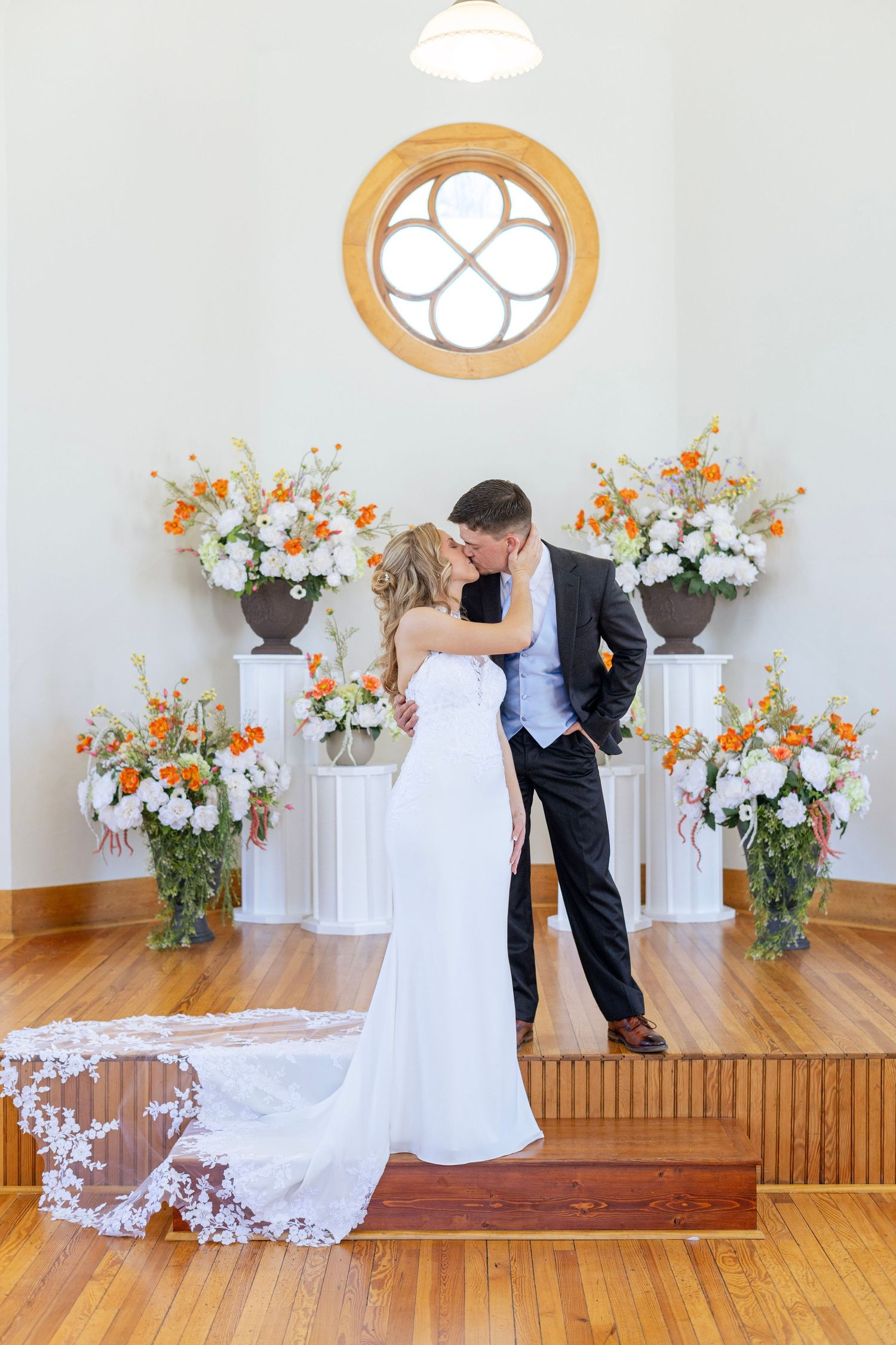 Bride and groom share a first kiss at the altar of a white chapel surrounded by orange and white florals.