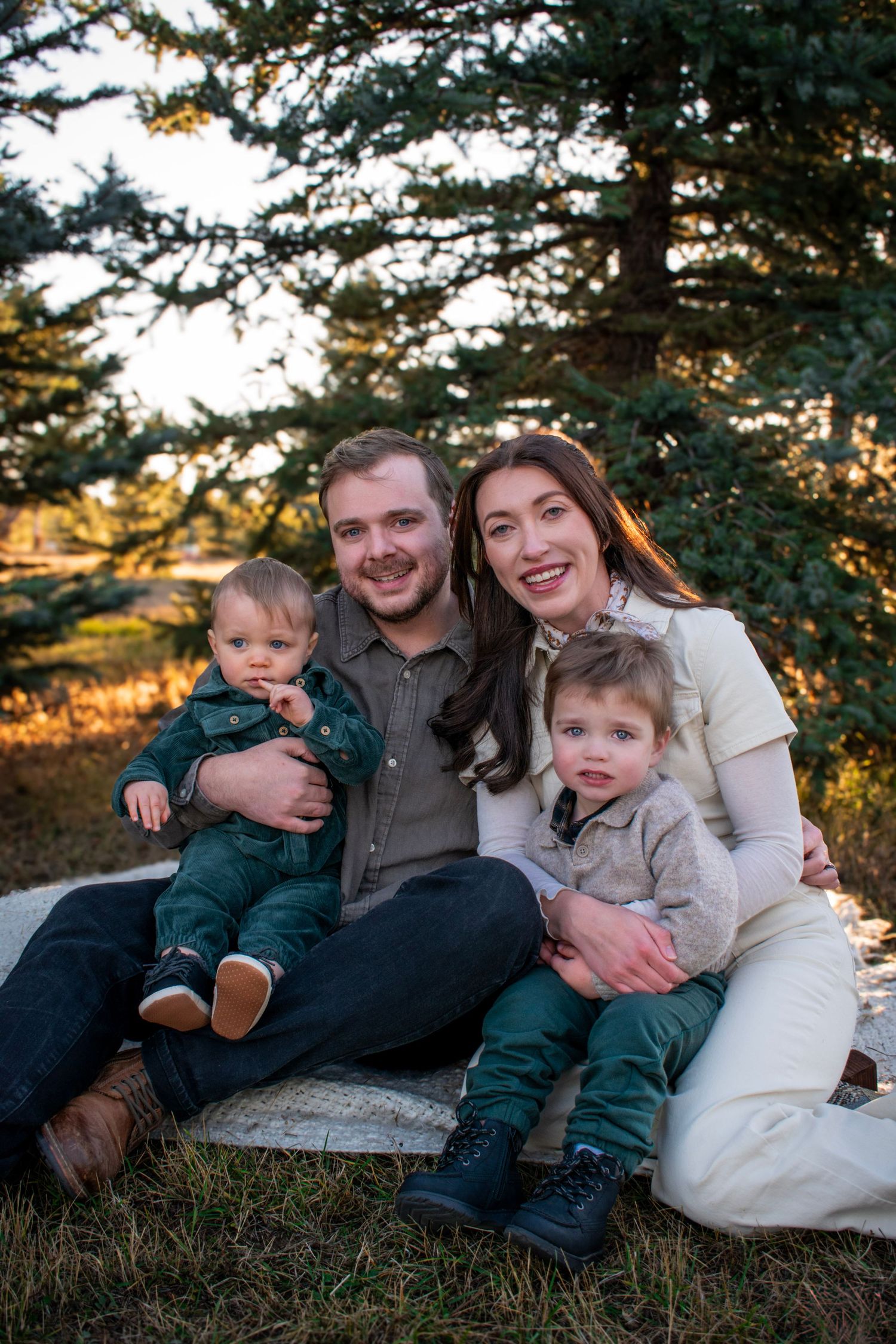 A relaxed family portrait session on a grassy hillside with pine trees at sunset.