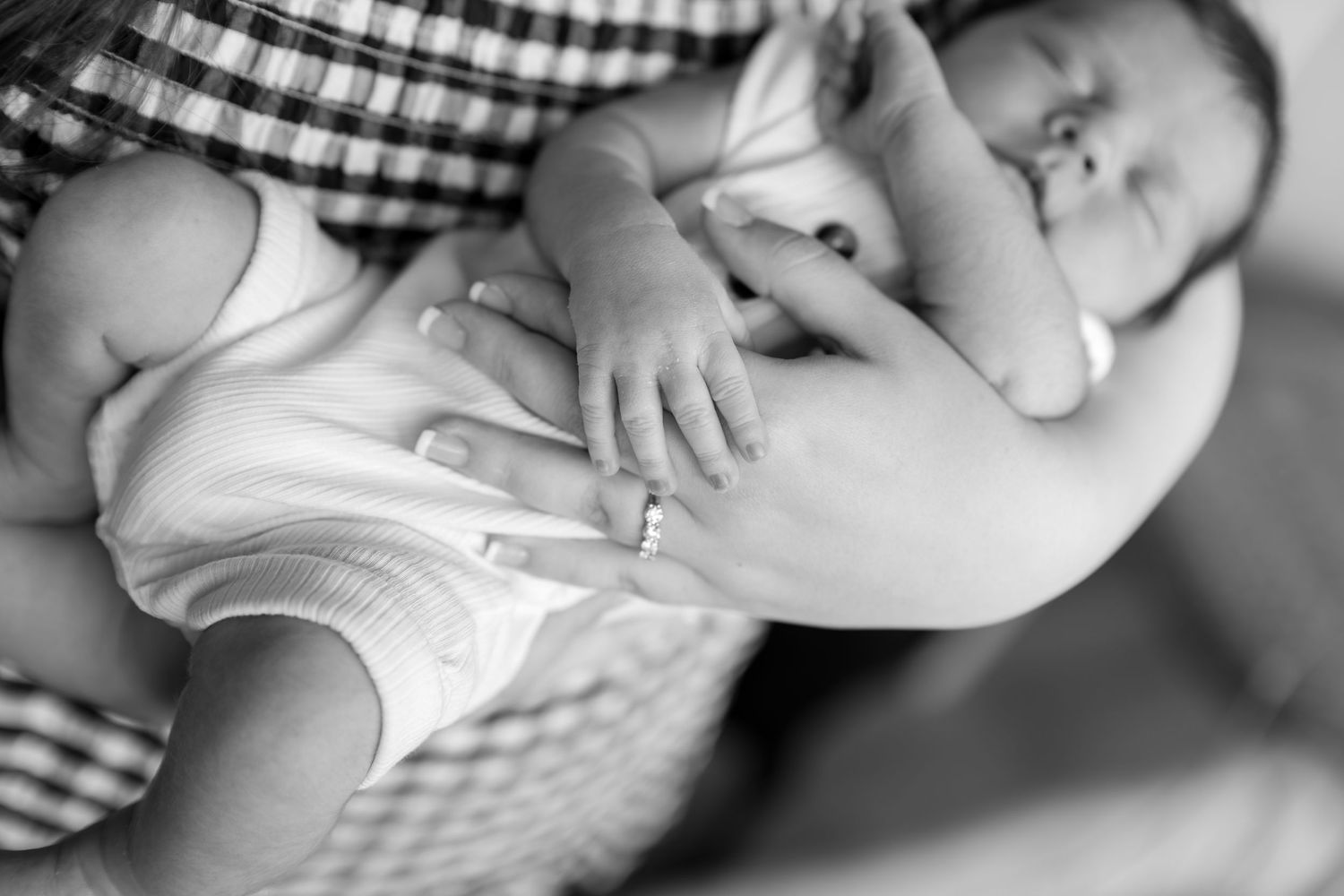 Black and white photo of a sleeping newborn baby cradled in a parent's arms, wearing a white onesie.