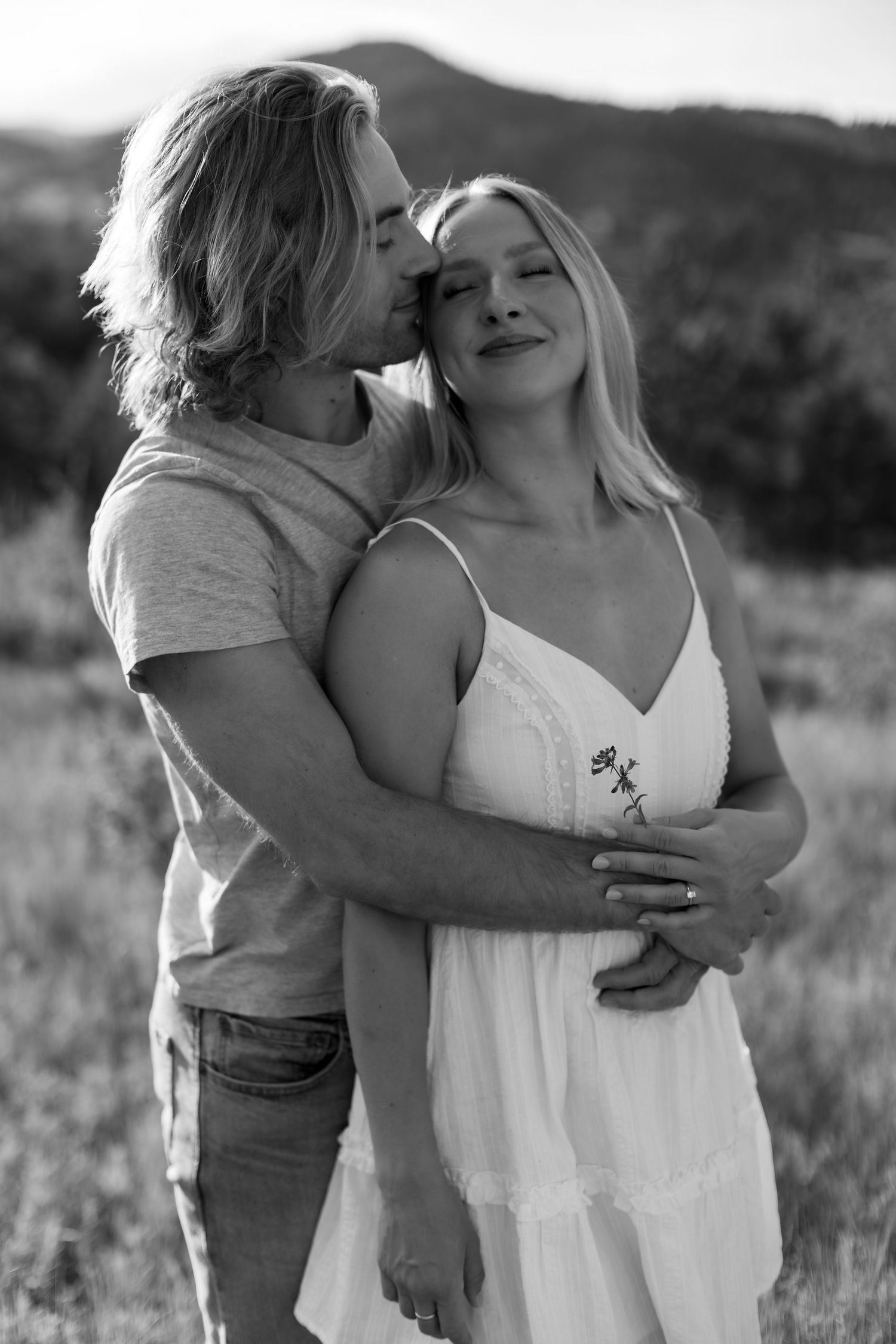 Black and white photo of a romantic couple embracing outdoors, man kissing womans temple.