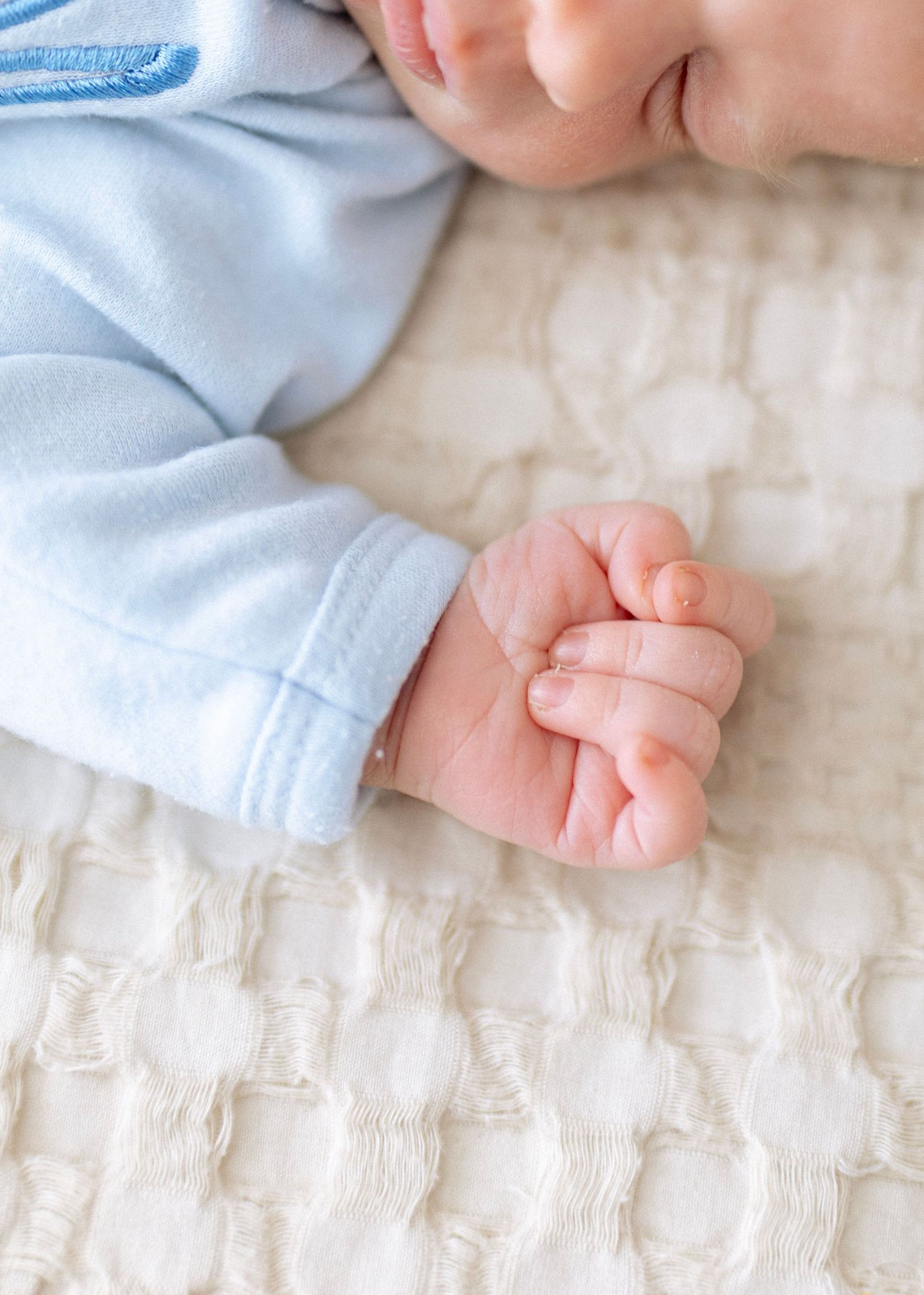 Close-up view of tiny baby feet and hands resting on a textured white blanket.