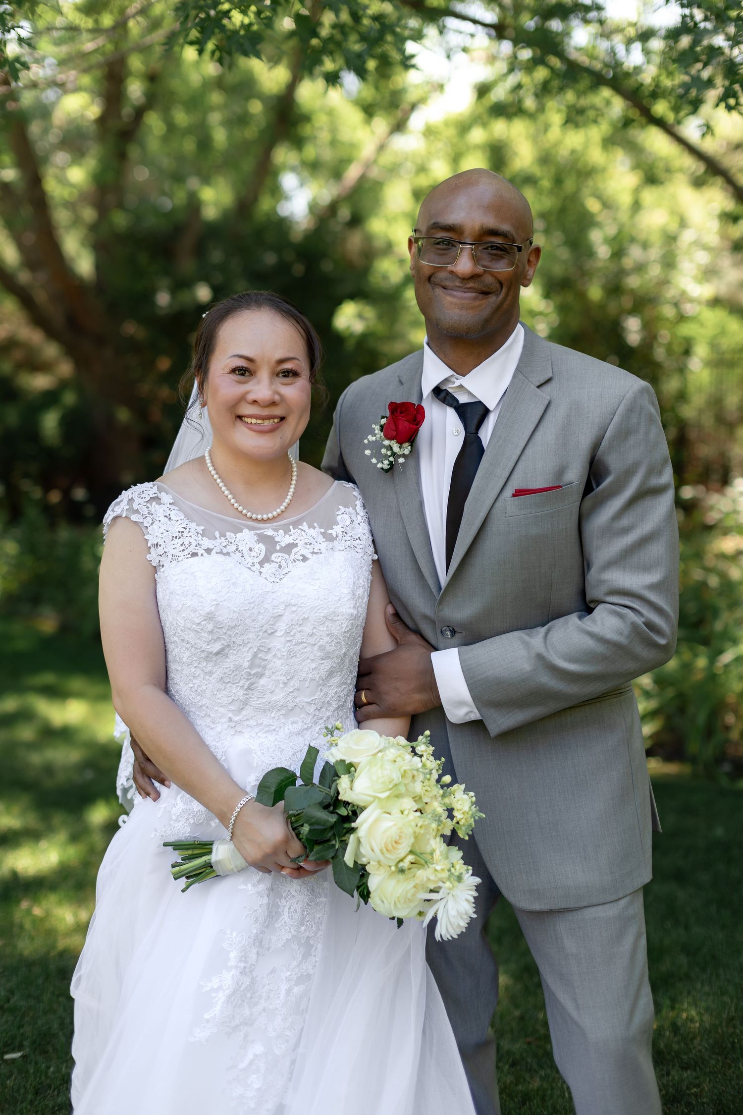 Smiling interracial bride and groom posing together in lush garden after wedding ceremony.
