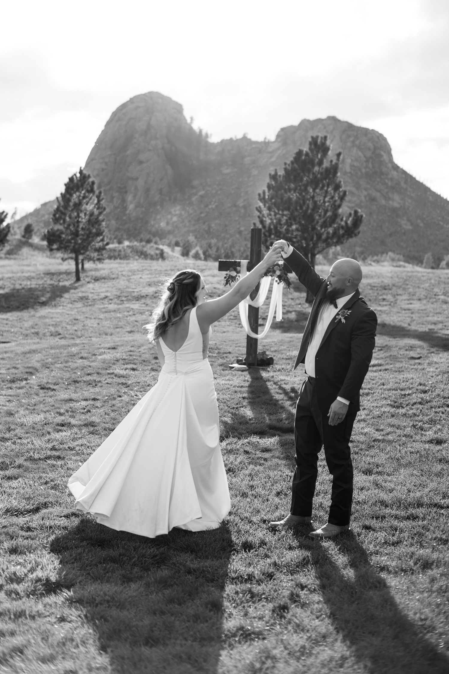 Black and white photo of bride and groom dancing outdoors with rocky mountain backdrop at elegant wedding ceremony.