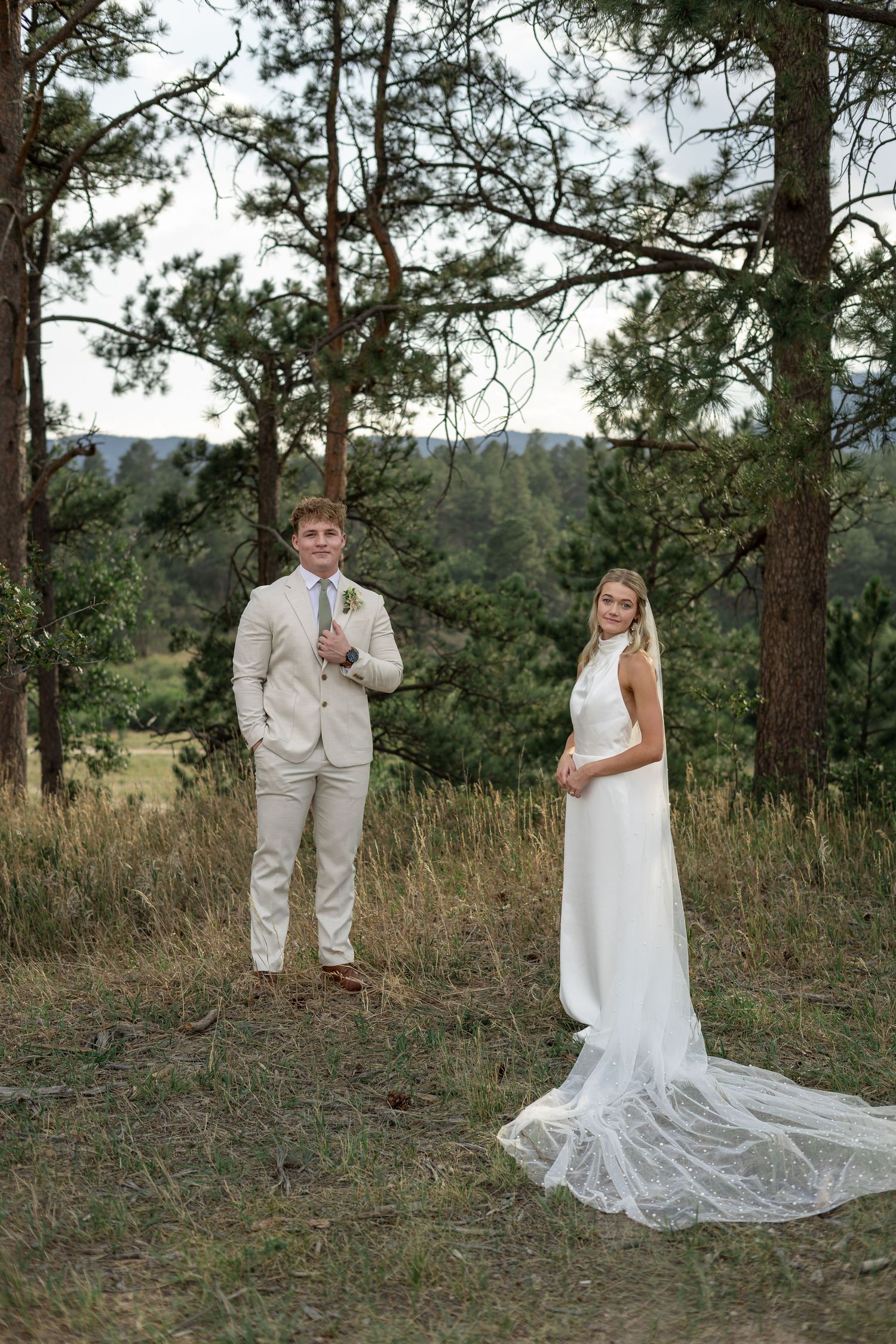 Bride and groom pose separately among tall pine trees in Colorado mountain wedding portrait.