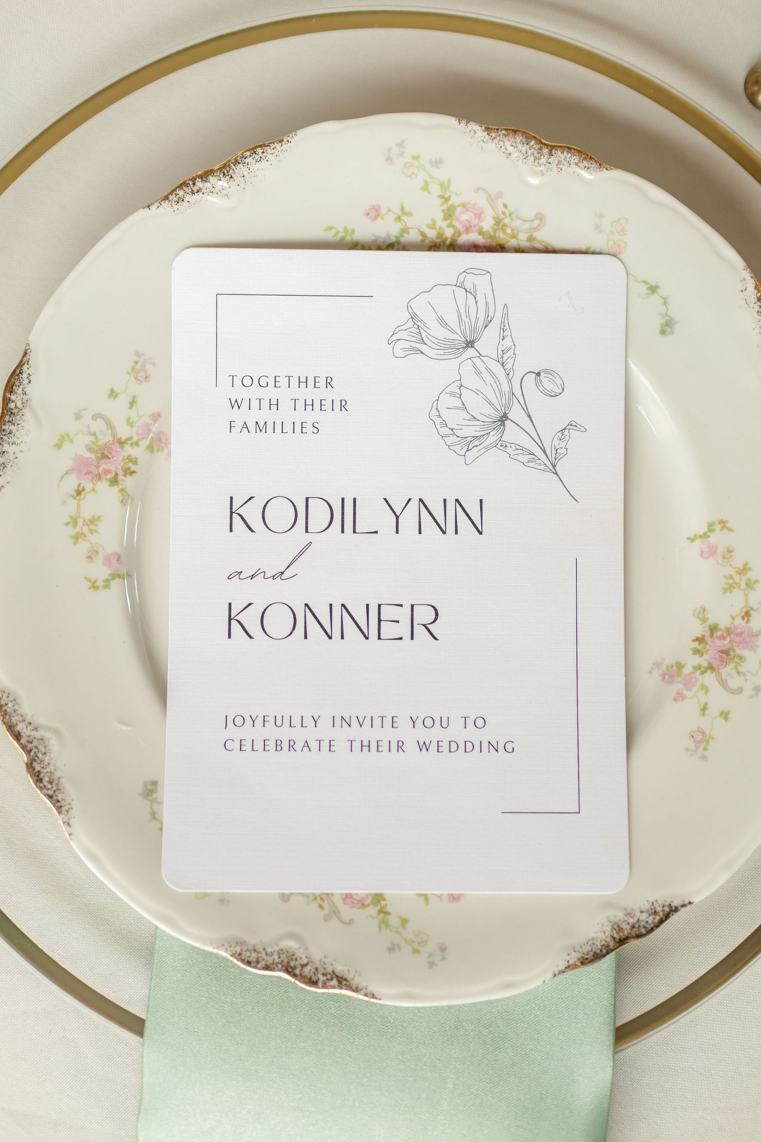 Wedding invitation for Kodilynn and Konner placed on vintage floral china plate with mint green napkin.