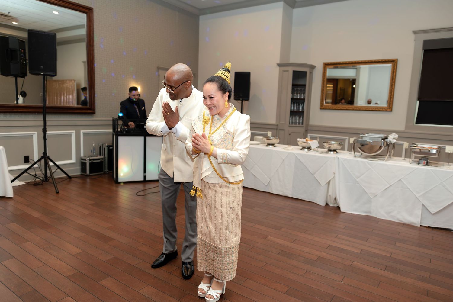 Couple in traditional Thai attire performing a ceremonial dance at an elegant indoor wedding reception.