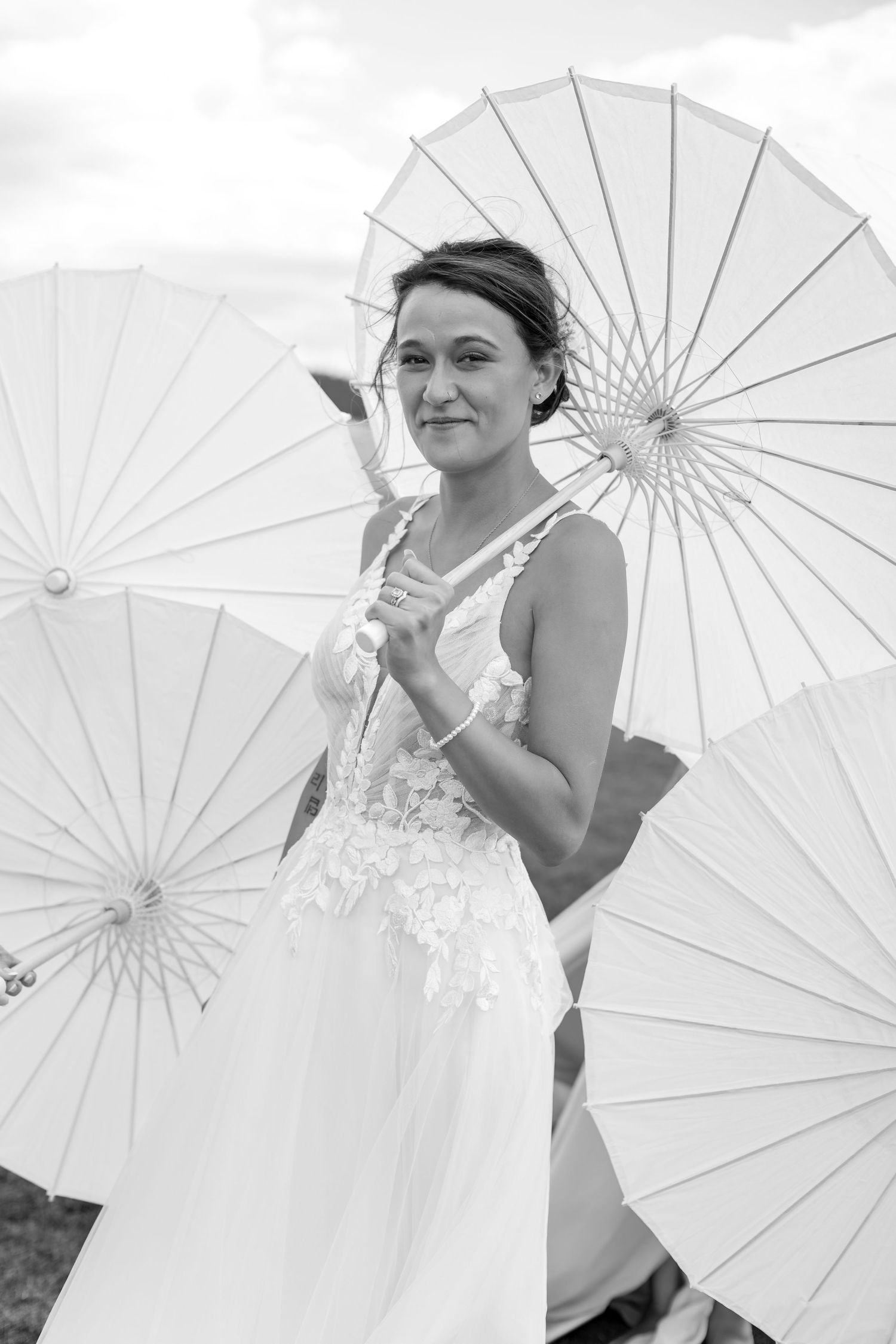 Black and white portrait of bride in lace gown holding white parasol at outdoor wedding.