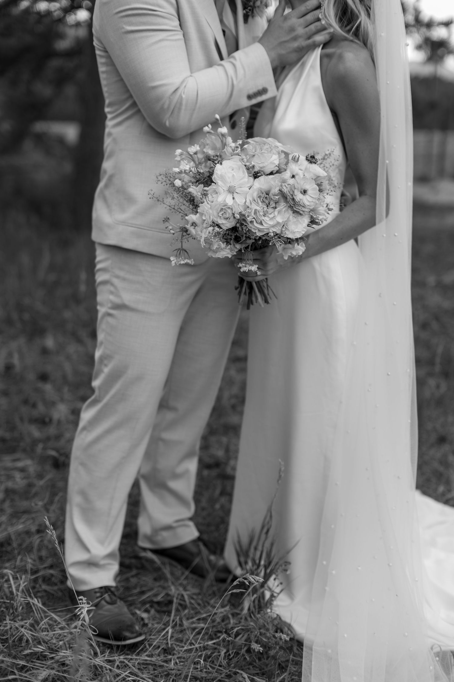 Black and white photo of a bride and groom embracing outdoors, bride holding a bouquet of roses.