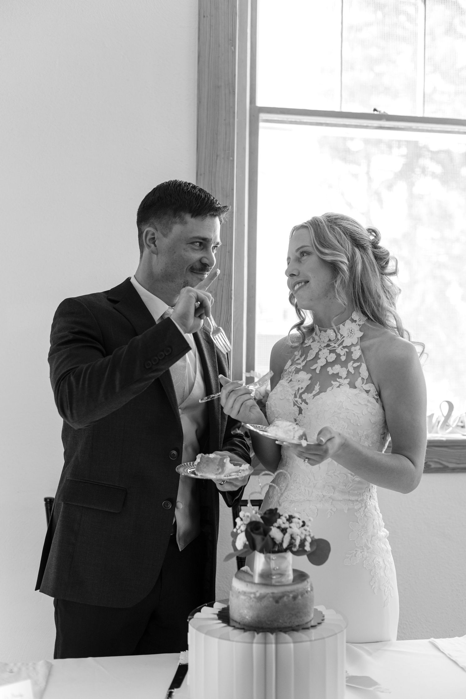 Black and white photo of bride and groom laughing while cutting their wedding cake together.