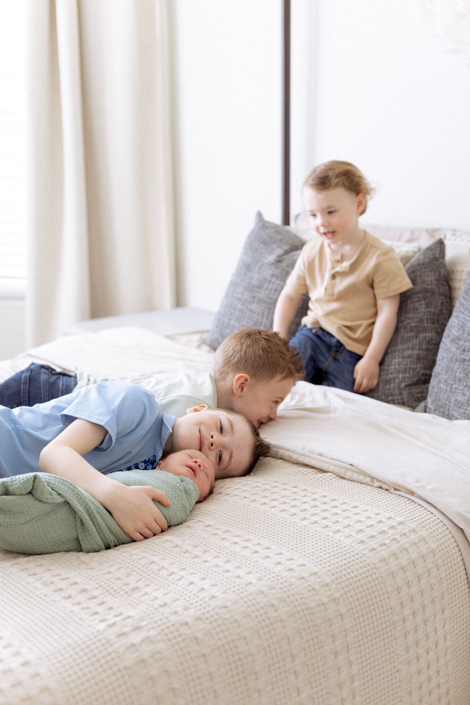 Children laughing and playing together on a cozy white bed with textured bedding and gray pillows.