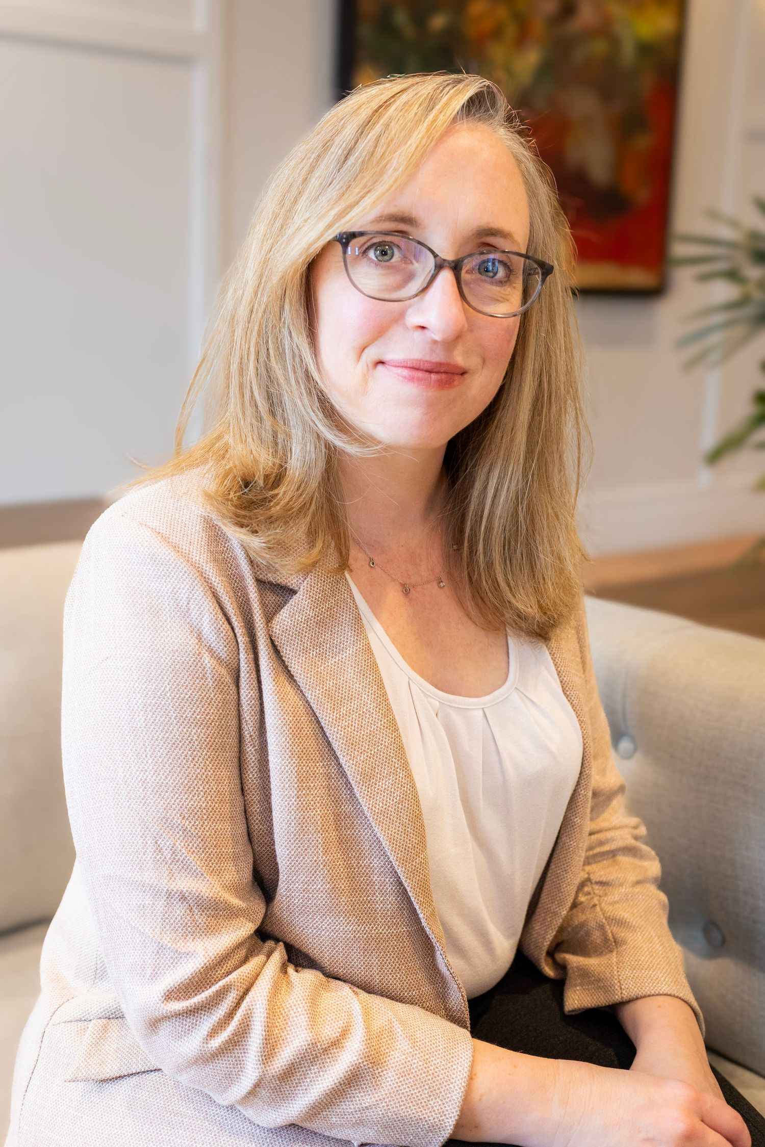 Professional headshots showing someone in a beige blazer and white top sitting at a desk with natural lighting.