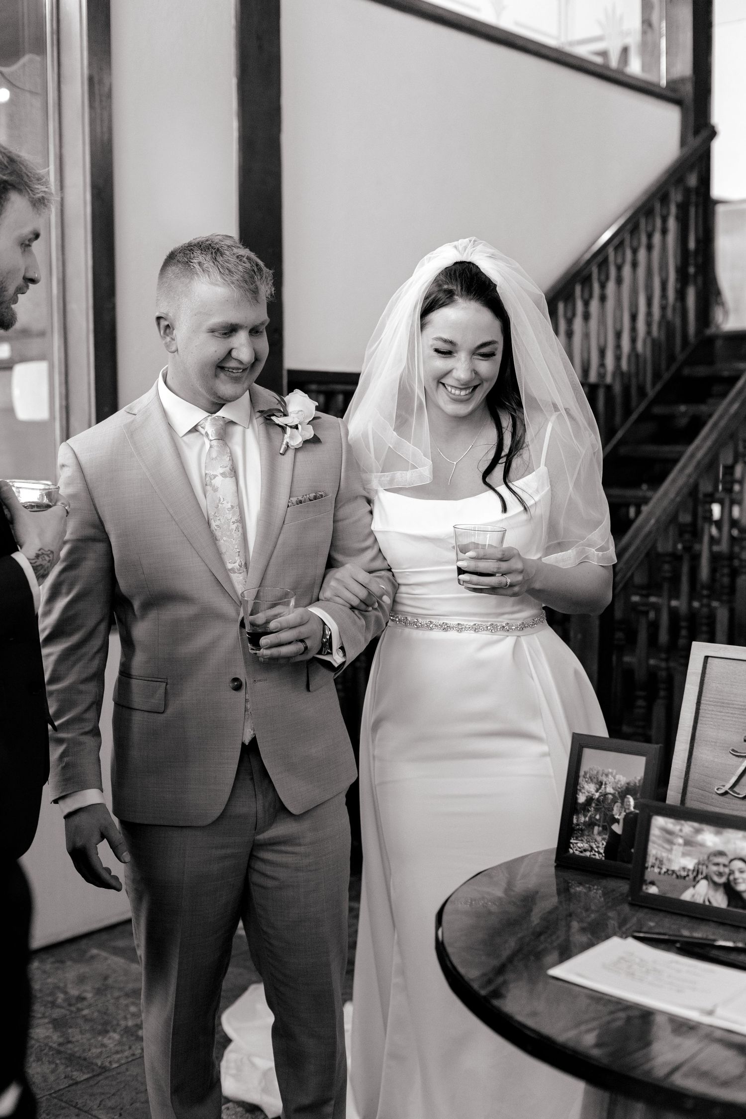 Black and white photo of smiling bride in veil and groom in gray suit at wedding reception.