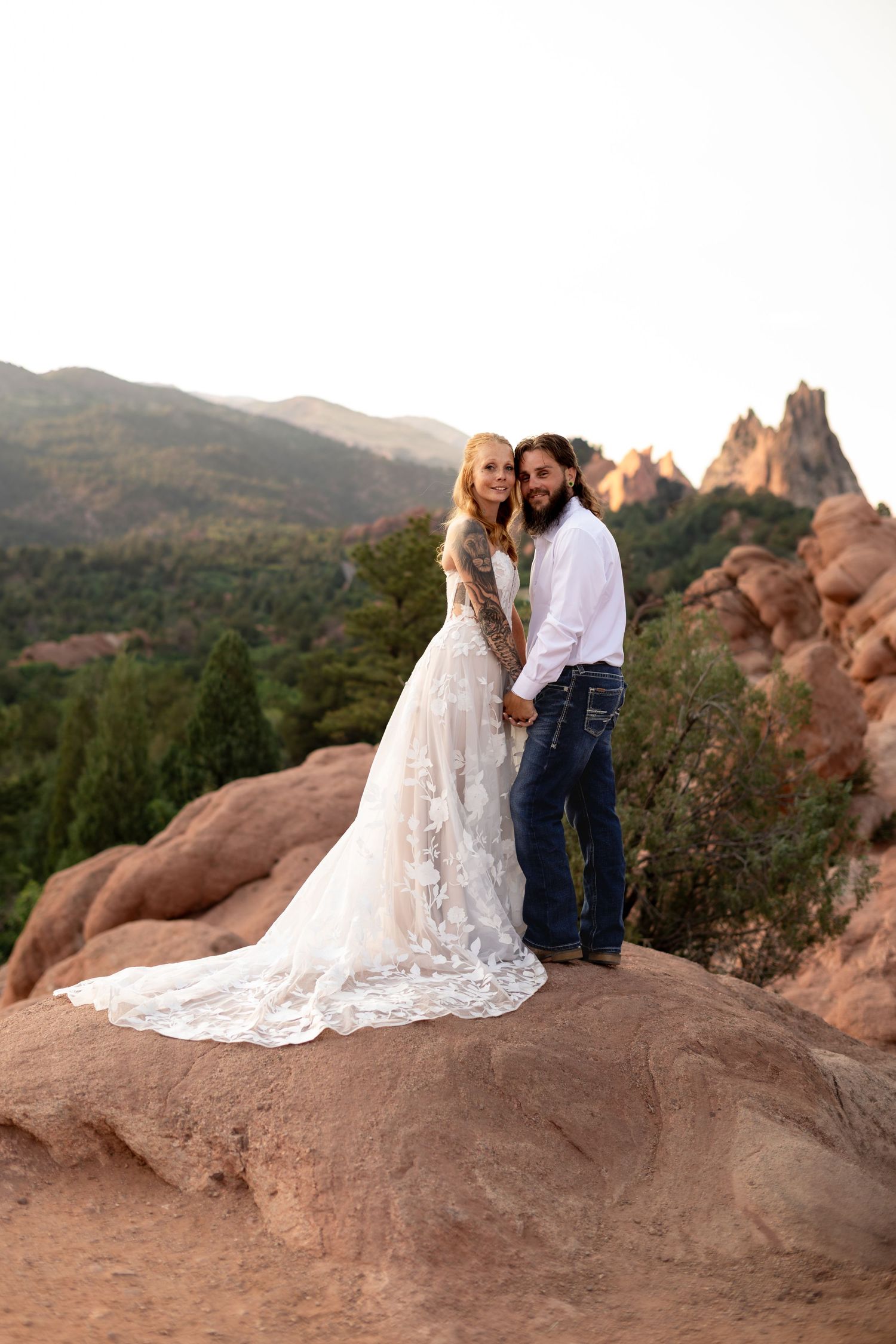 Bride and groom stand on red rocks at Garden of the Gods, Colorado, with mountain views behind them.