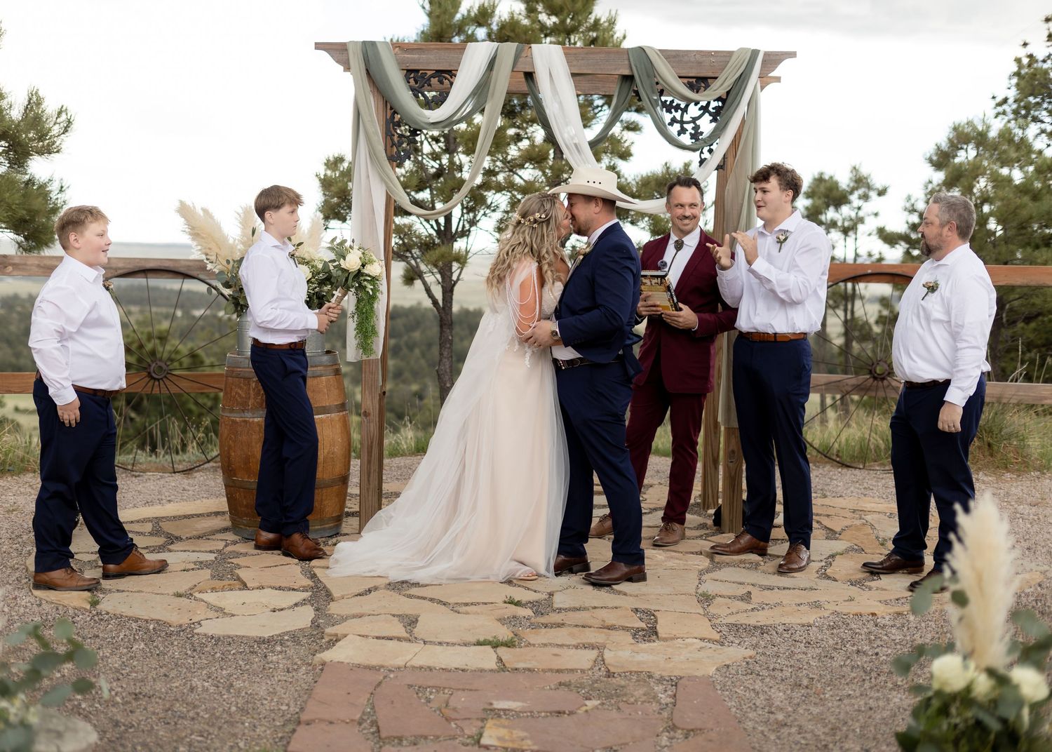 Bride and groom exchanging vows at rustic outdoor ceremony with wedding party gathered around.