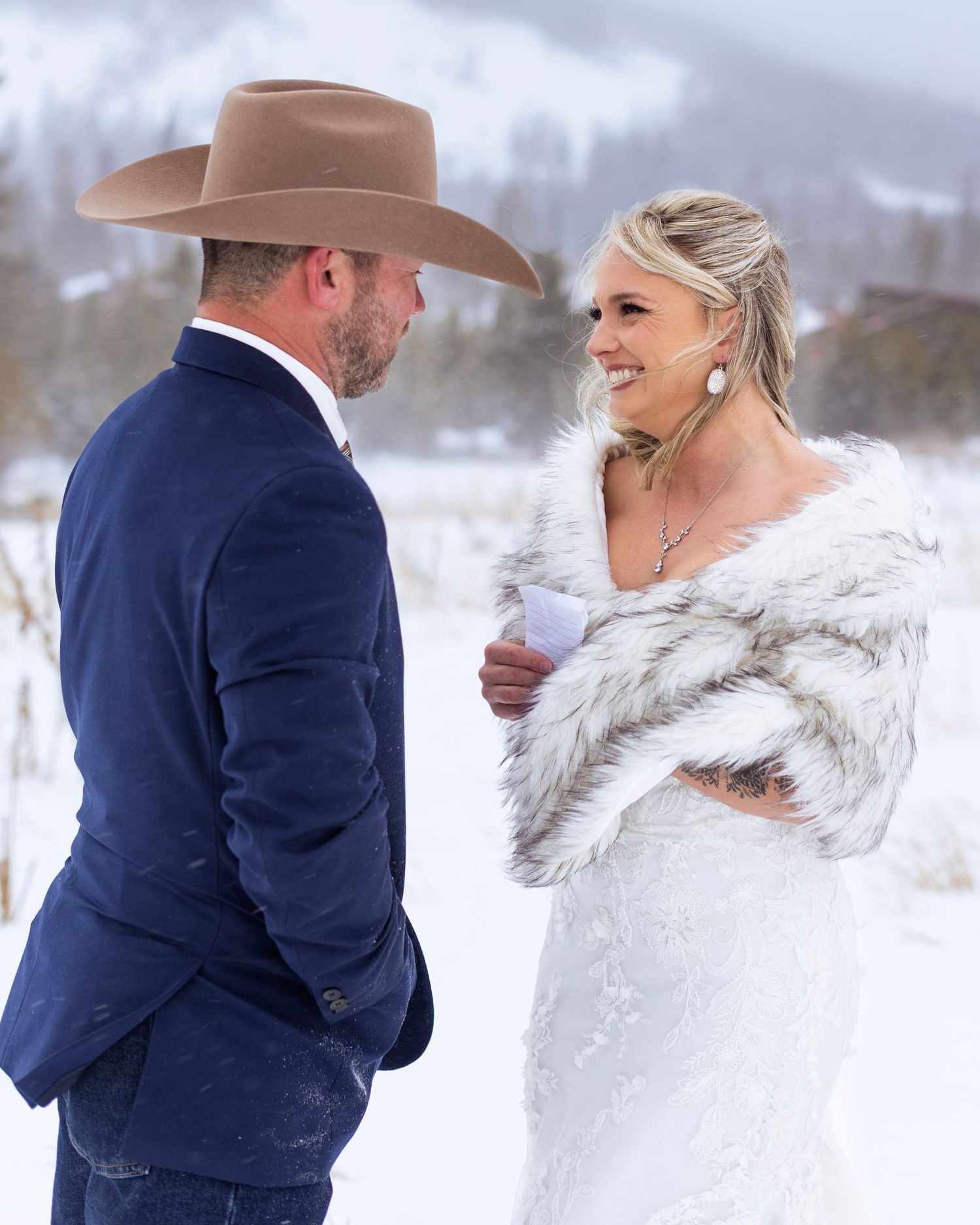 A couple in winter wedding attire shares a romantic moment in the snow with the bride wearing a white fur wrap.