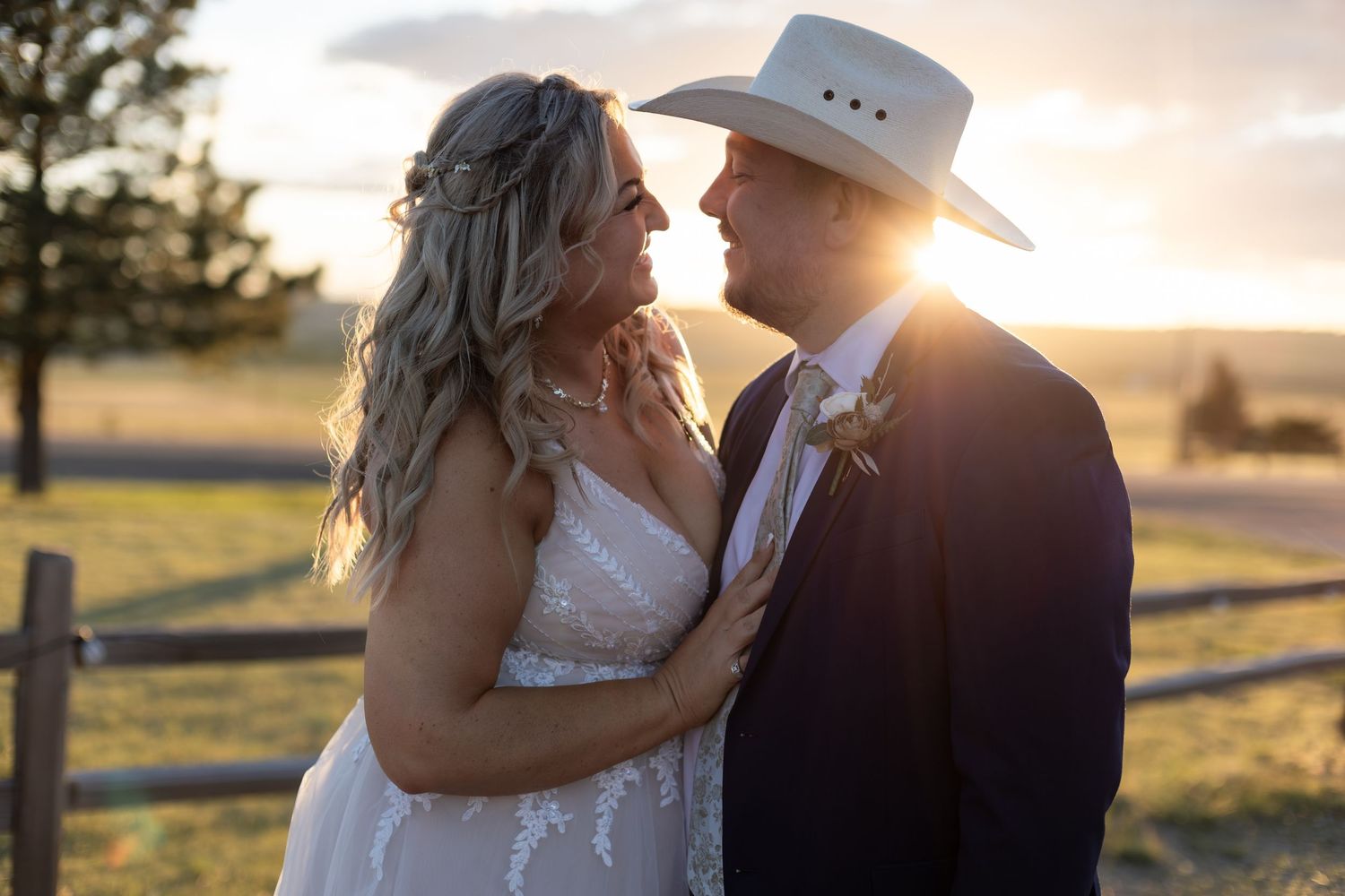 Bride and groom in cowboy hat share a romantic golden hour moment by a ranch fence.