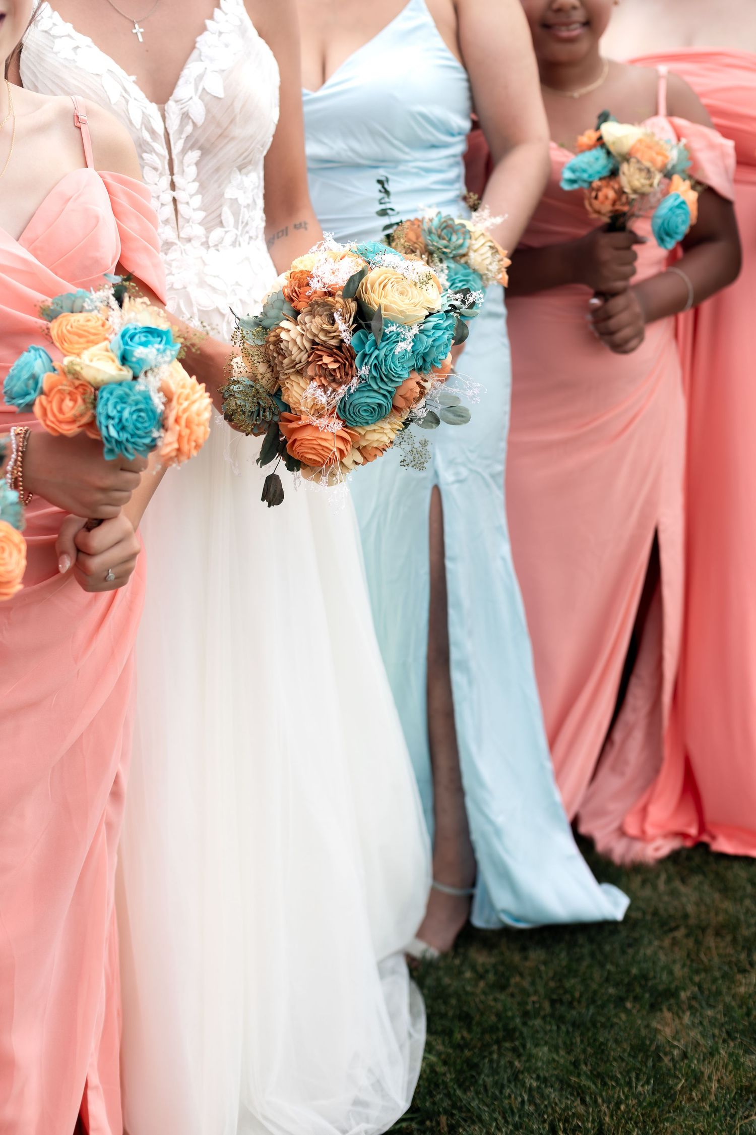 Bride in white gown with bridesmaids in coral and blue dresses holding teal and orange floral bouquets at wedding.