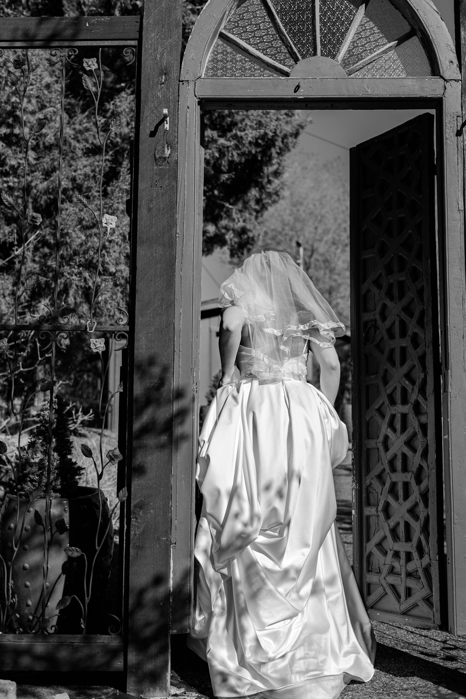 Black and white photo of bride in white gown and veil walking through elegant doorway.