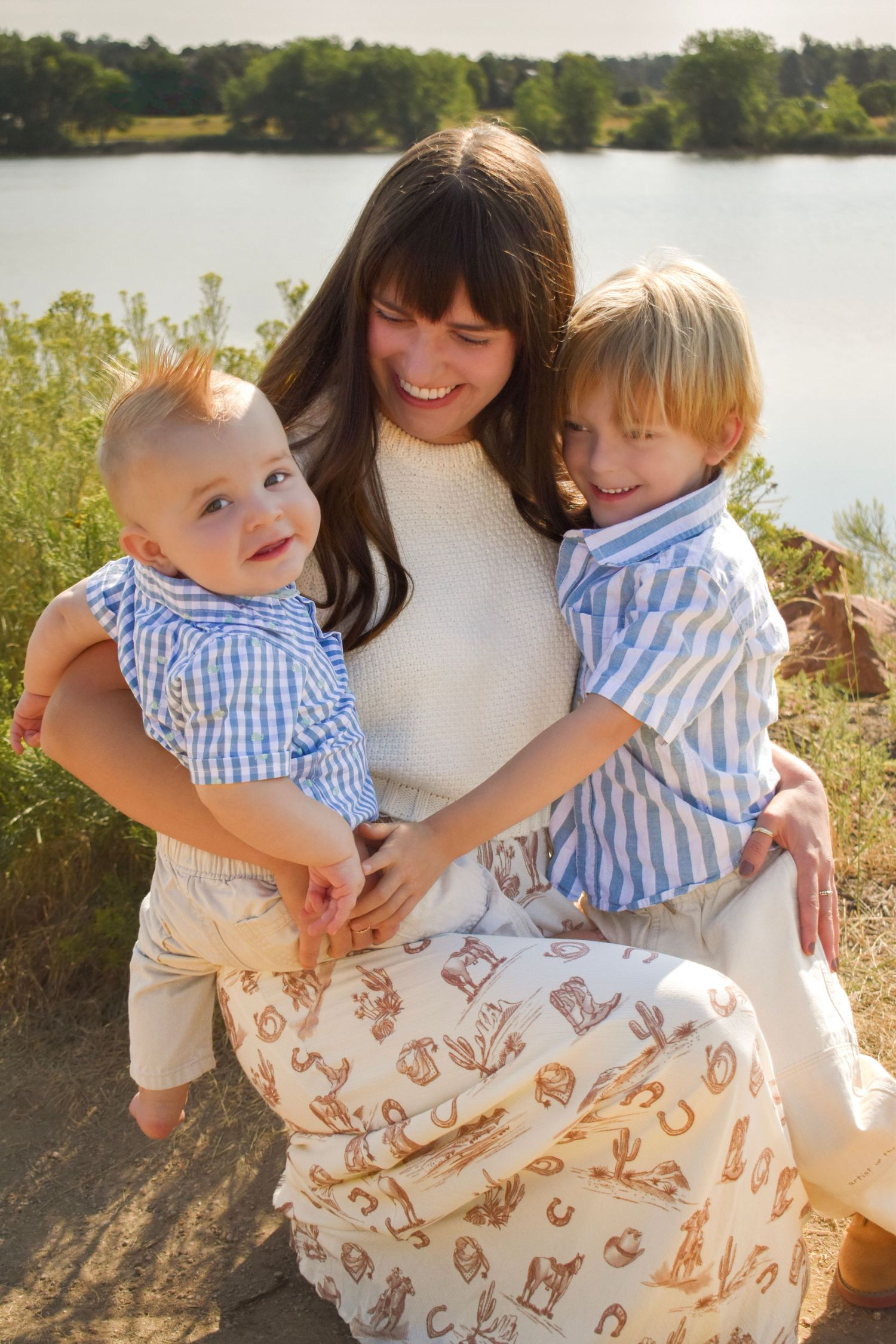 A family wearing coordinated blue and white outfits sits together by a lake during a golden hour photoshoot.