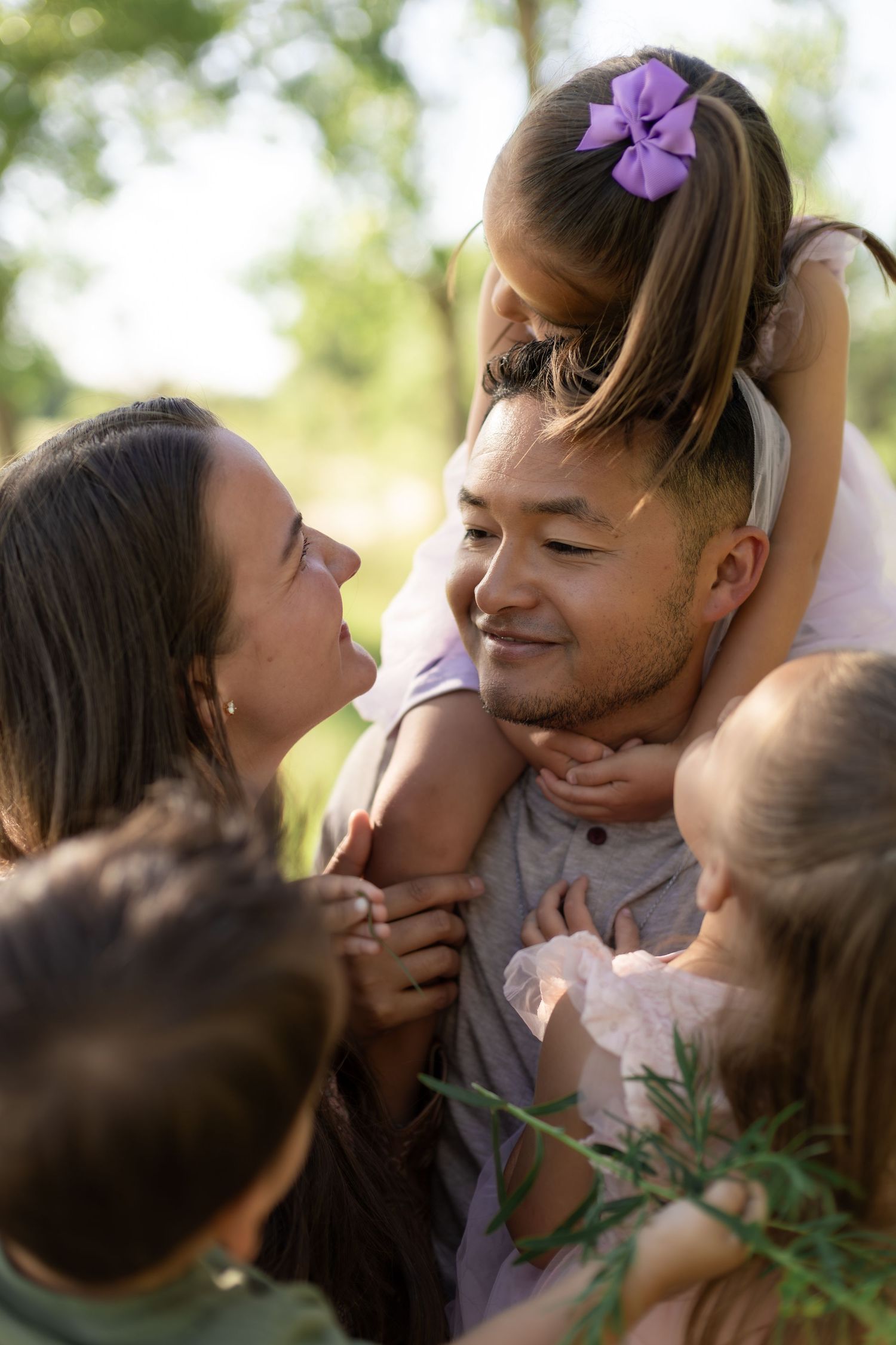 Happy multiracial family with children enjoying a sunny day outdoors, father carrying daughter on shoulders.