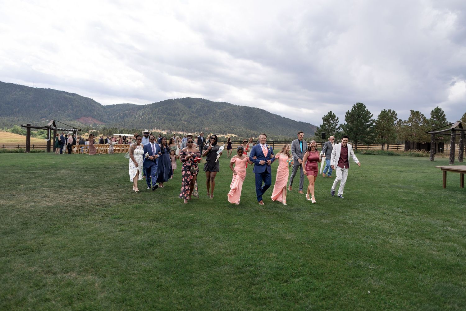 Wedding guests walk across green lawn at outdoor mountain ranch reception under cloudy skies.