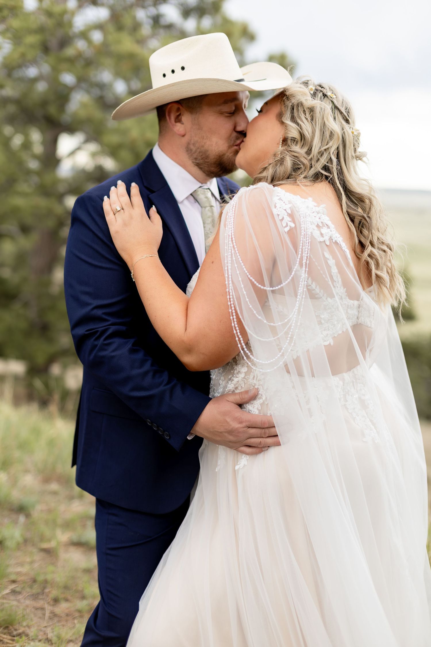Groom in navy suit and cowboy hat shares a tender kiss with bride in lace wedding gown.