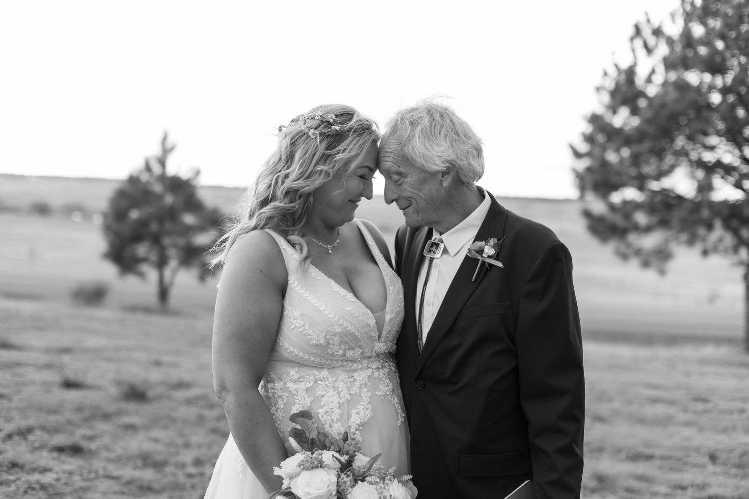 Black and white photo of a bride and groom sharing an intimate moment outdoors at a rustic wedding.