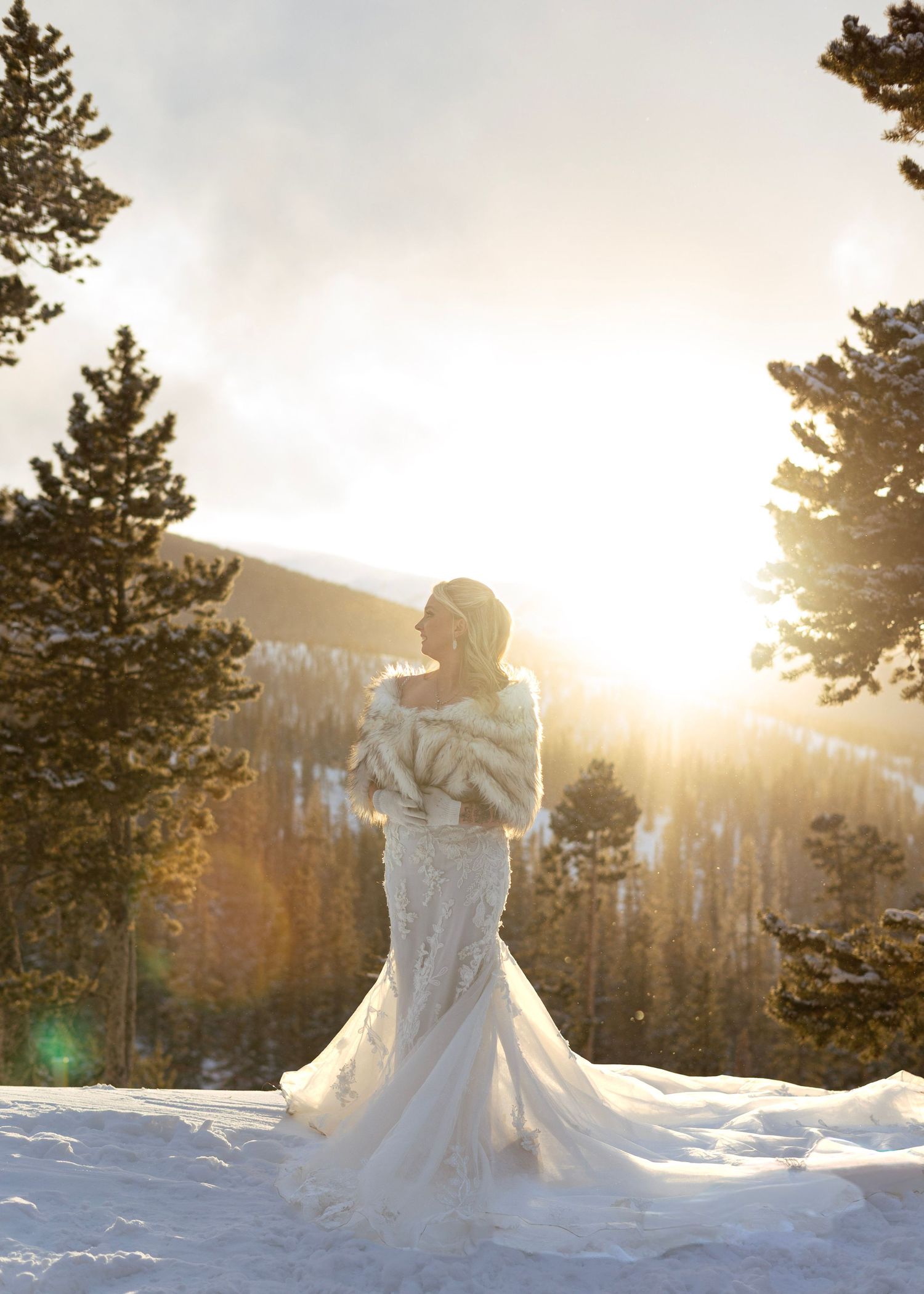 A white dress twirls in golden sunlight against a snowy mountain backdrop with evergreen trees.