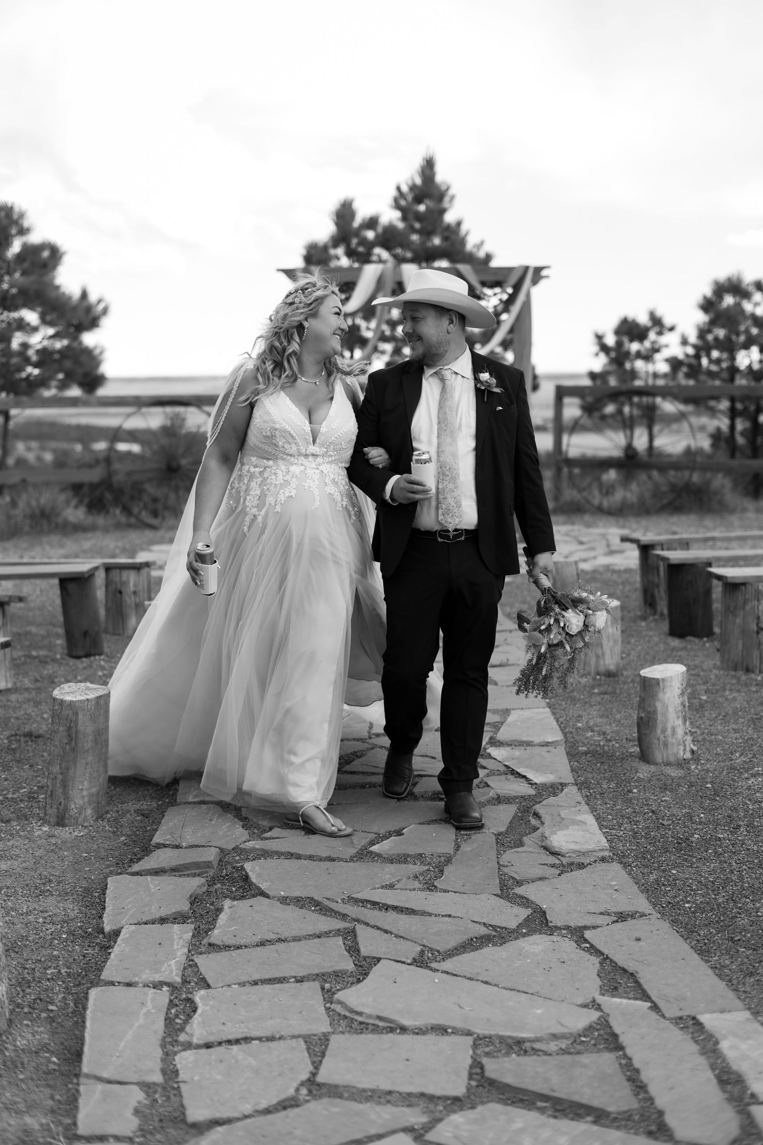 Black and white photo of bride and groom walking down stone aisle at outdoor rustic wedding.