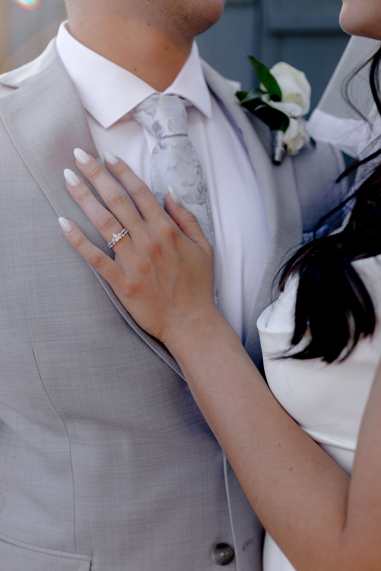 Close-up of bride's hand with diamond ring resting on groom's grey suit jacket during wedding ceremony.