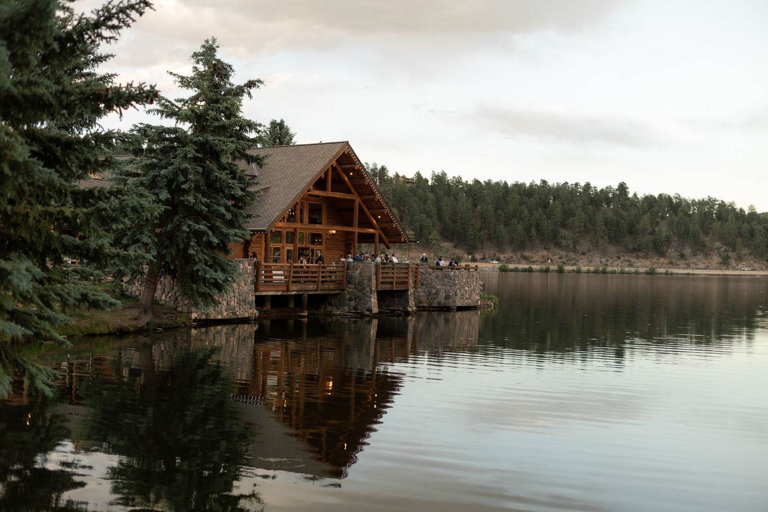Rustic wooden cabin on a calm lake reflecting pine trees at dusk in a serene forest setting.